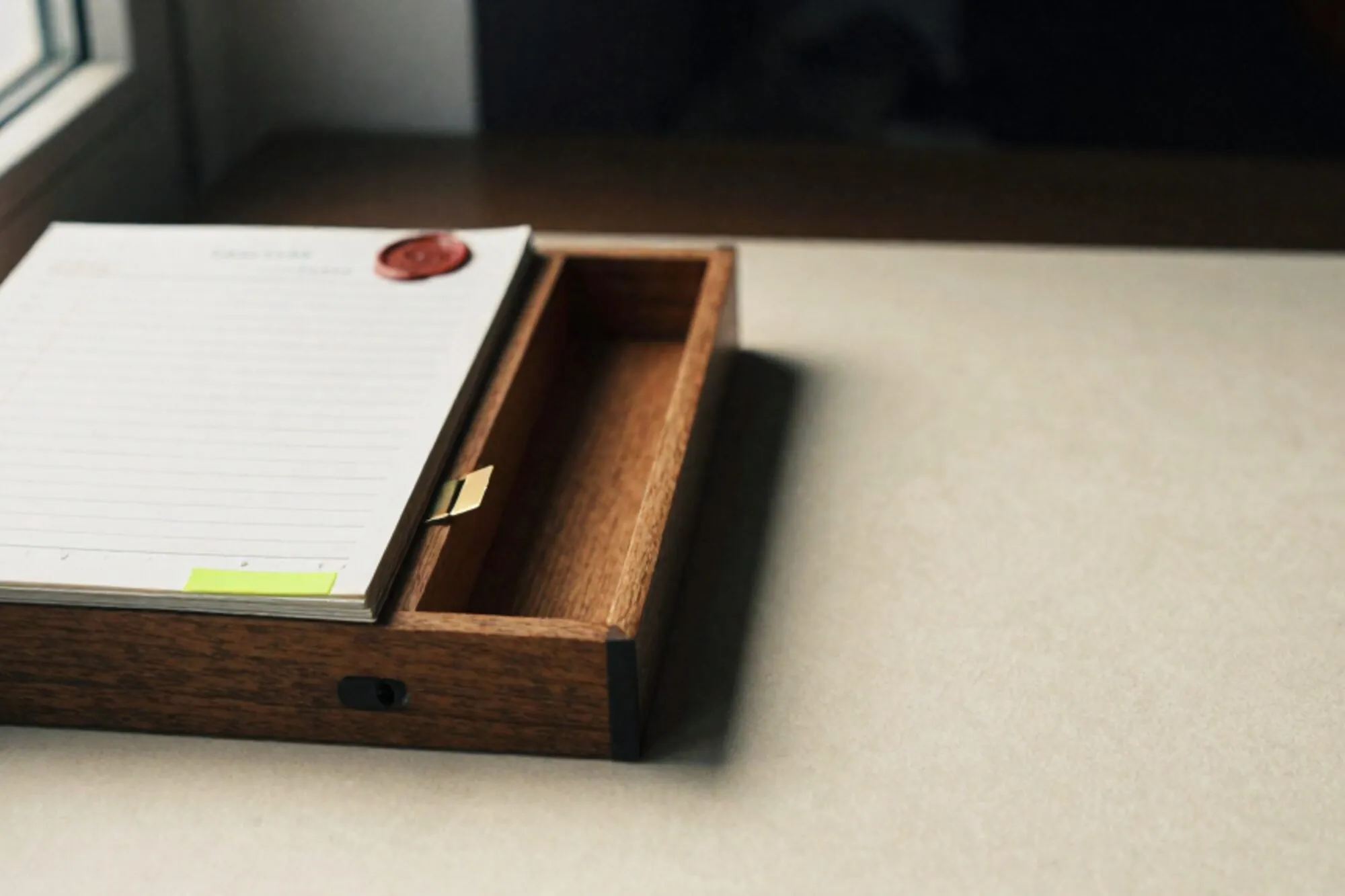 Open wooden index-card drawer with brass divider, ledger stack, chartreuse paper tab, red wax seal on ivory paper.