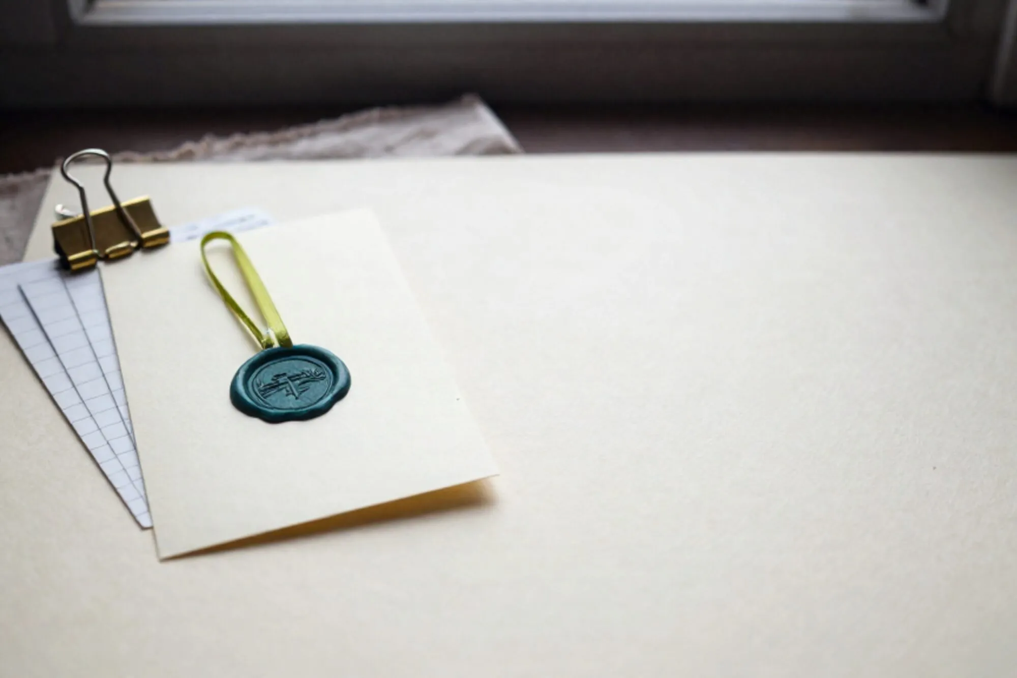 Crème mandaatkaart met groen waszegel, groen lint, koperen paperclip en twee grootboekstrookjes op linnen vloei.