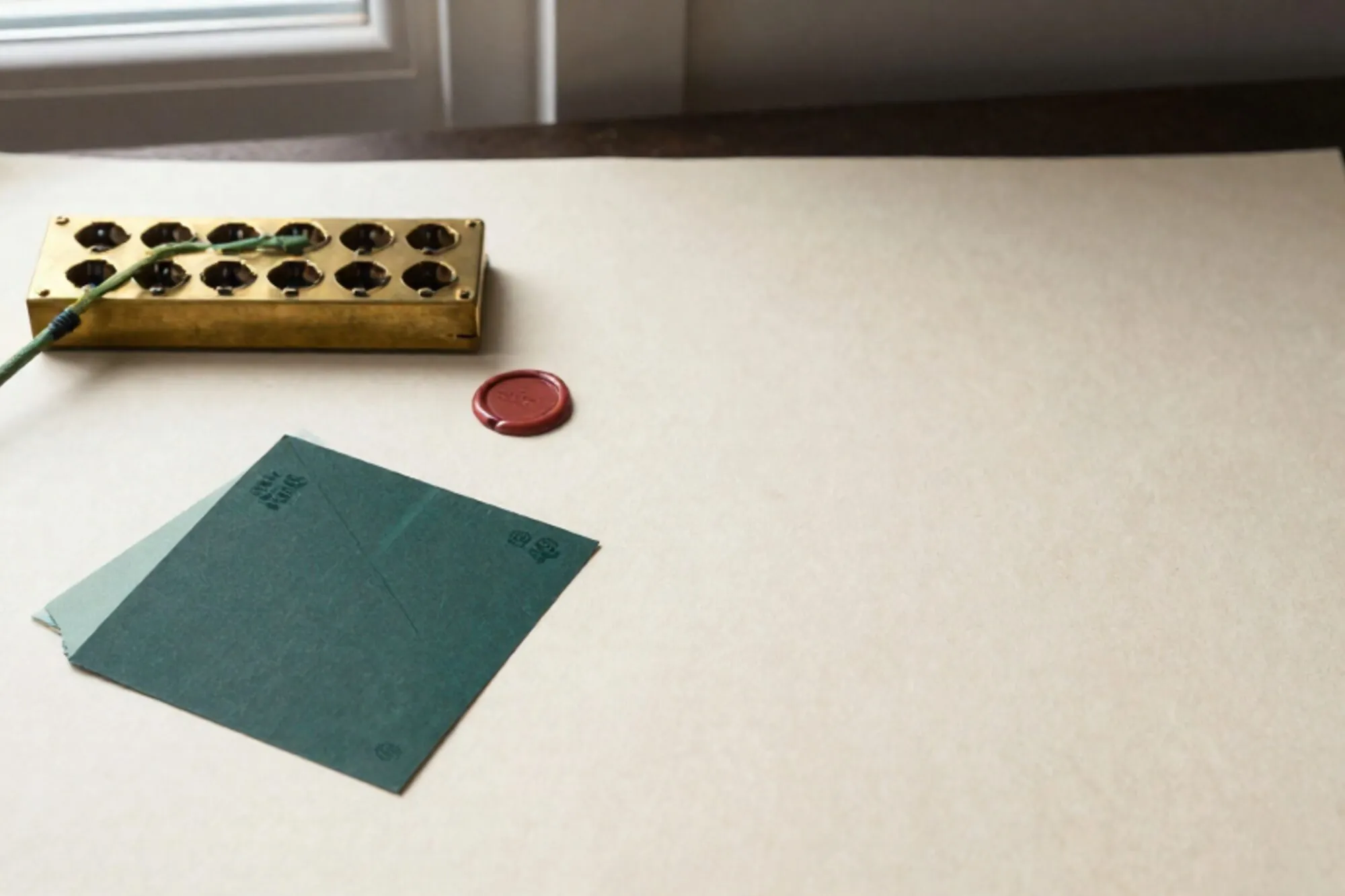 Brass switchboard with seventeen sockets on ivory desk blotter, one green patch cable, folded dark docket, red wax seal.