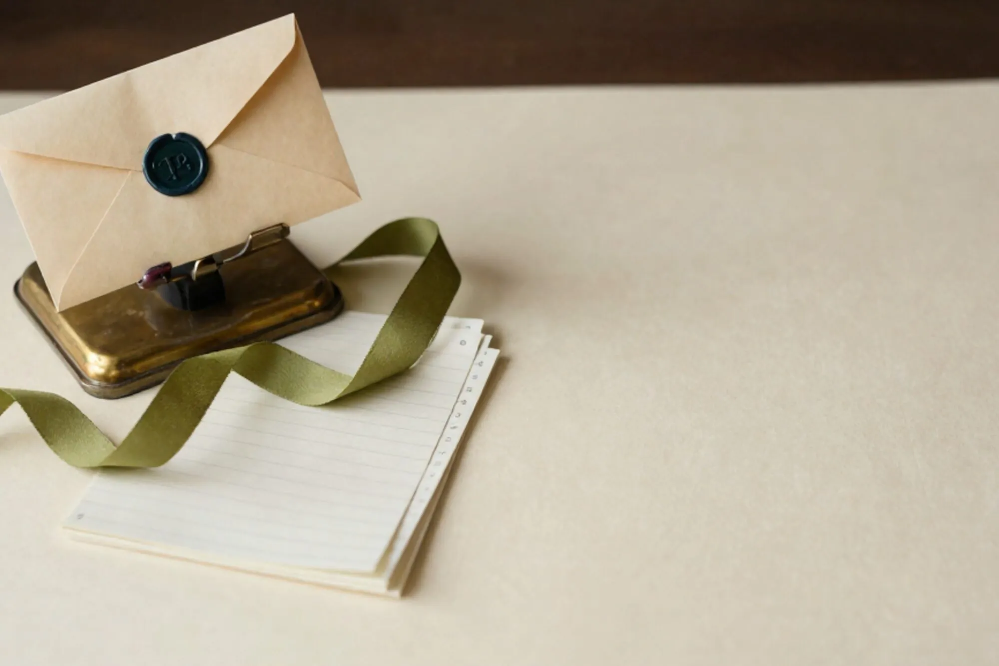 Brass postal scale with cream envelope sealed in green wax, ribbon and numbered ledger slips on ivory desk.
