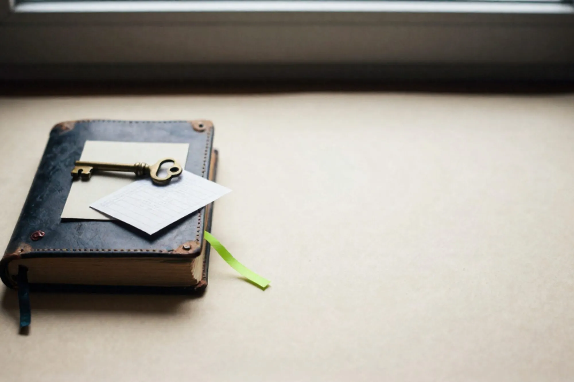 Closed leather logbook with brass key, cream index card, green ribbon, and red wax fragment on ivory paper.