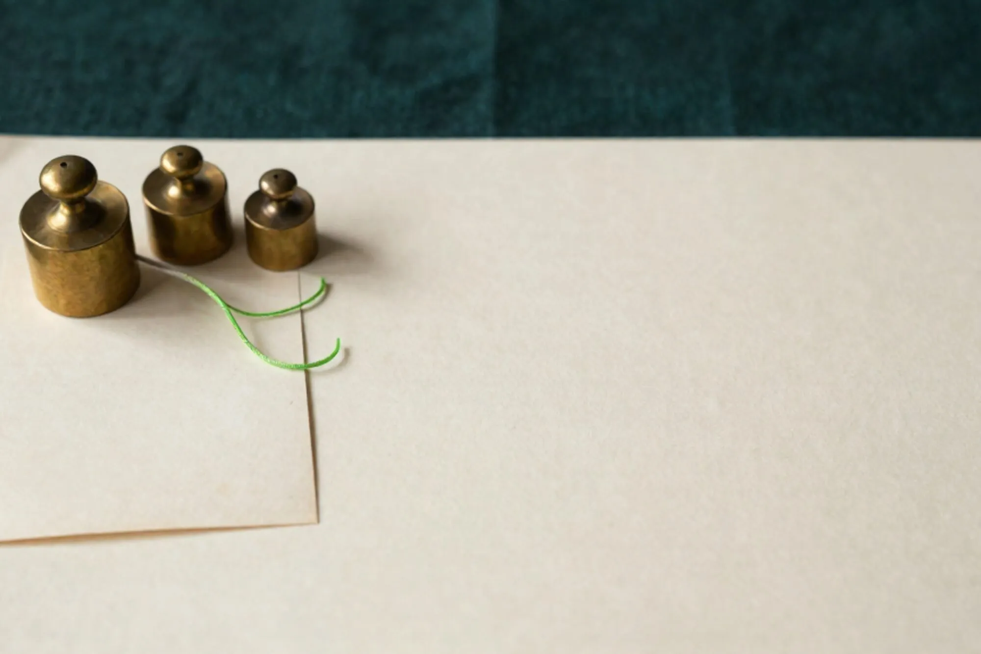 Three brass weights and a cream index card on ivory paper, chartreuse thread looping between them, forest linen edge.