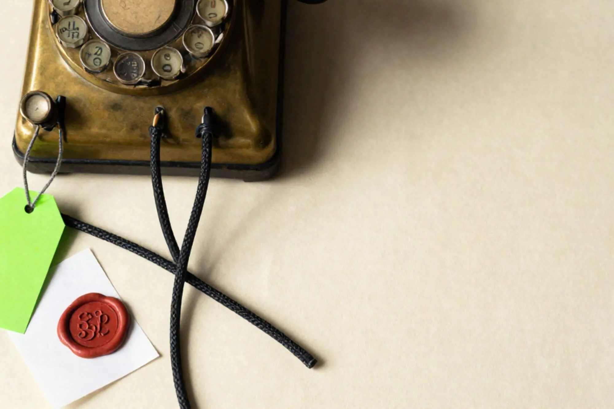 Brass telephone switchboard with twelve braided patch cables on ivory paper, one green tag, red wax seal on a folded docket.