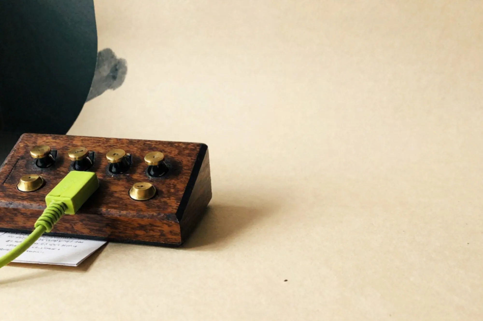 Houten telefooncentrale met messing hendels en één groen patchsnoer op ivoorpapier, diepe schaduwen, lege rechterkant.