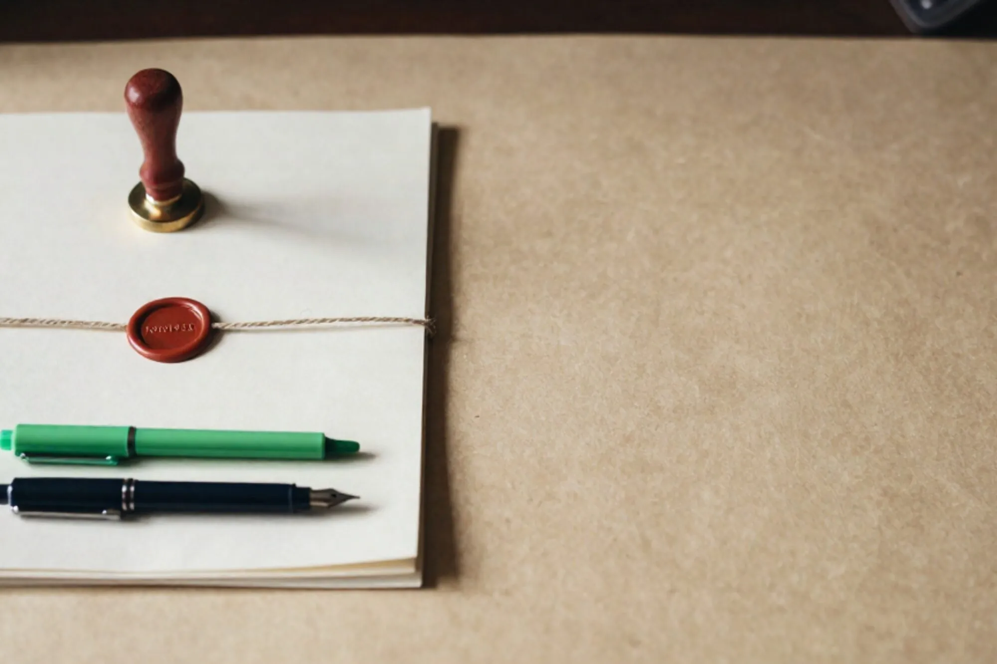 Folded ivory contract tied with twine, red wax seal, brass paperweight, green ribbon, dark fountain pen on desk.
