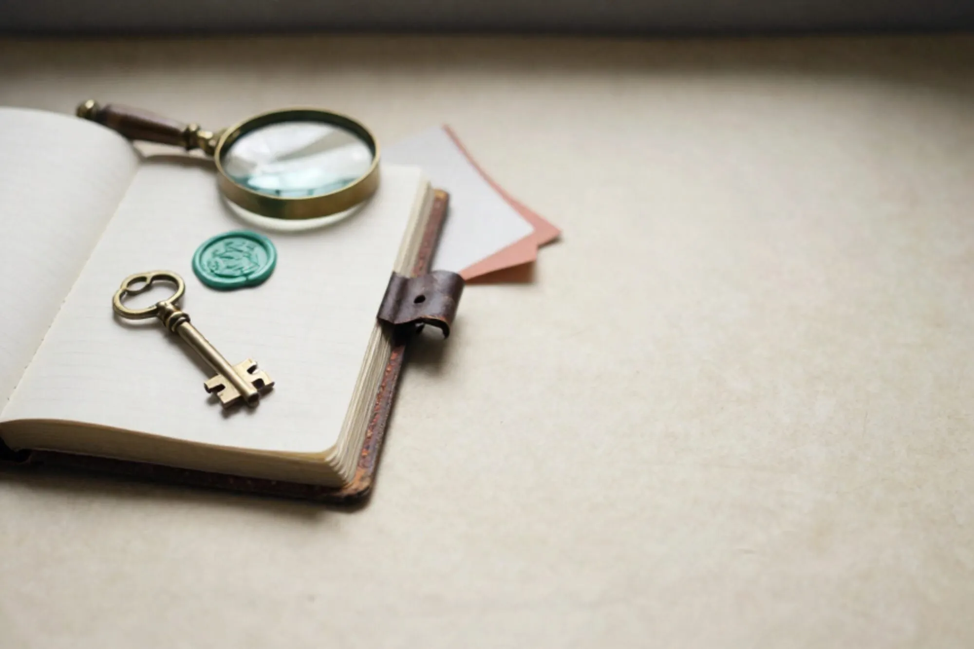 Half-open leather ledger with brass key, green wax seal, brass loupe and folded carbon slip on ivory paper surface.