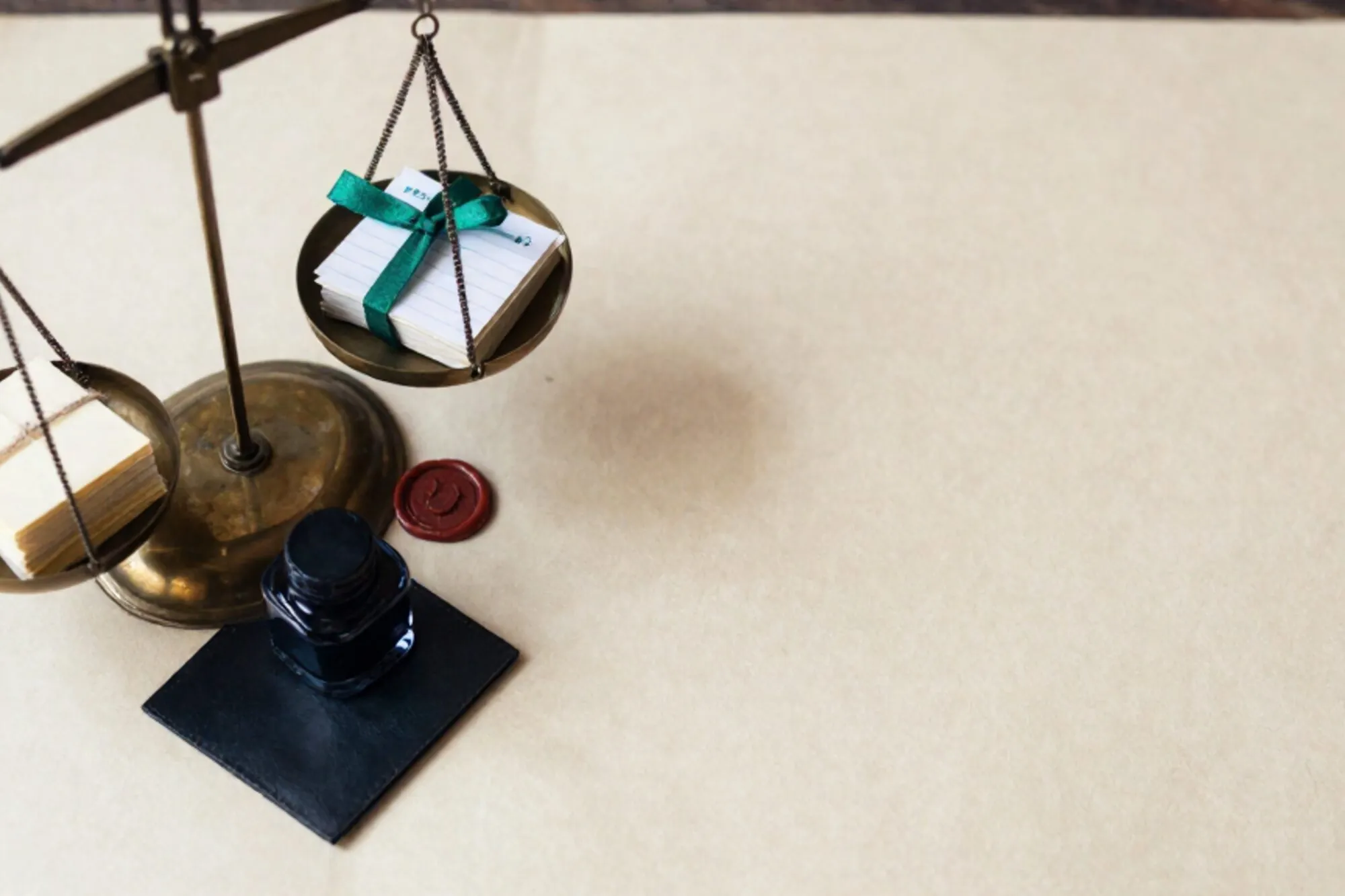 Brass balance scale on ivory paper, paper slips with twine on one pan, ledger card with green ribbon on other, red wax seal.