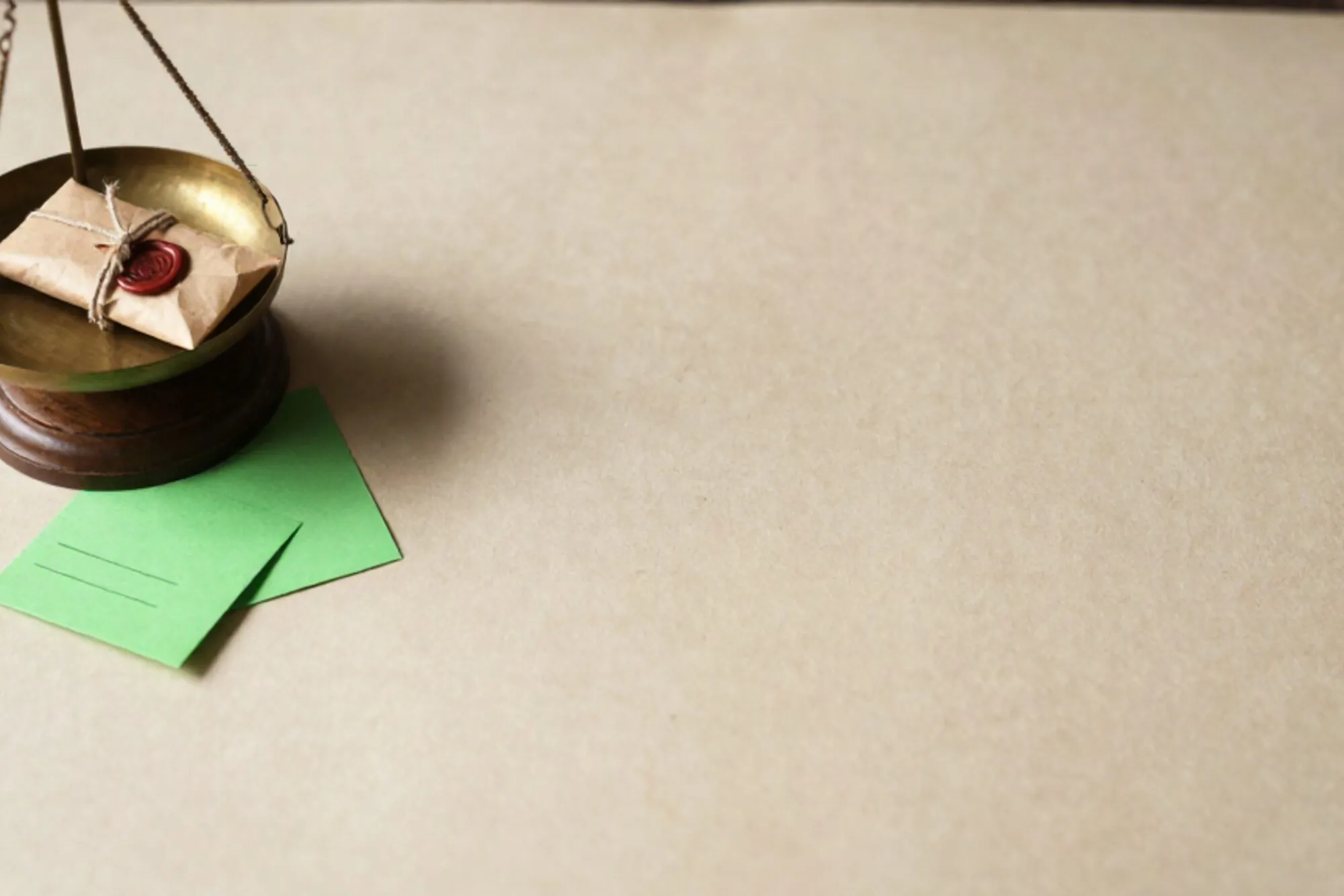 Antieke koperen weegschaal op ivoren bureauvloei met klein pakketje, linnen touw, rode lakzegel en groene briefkaart.