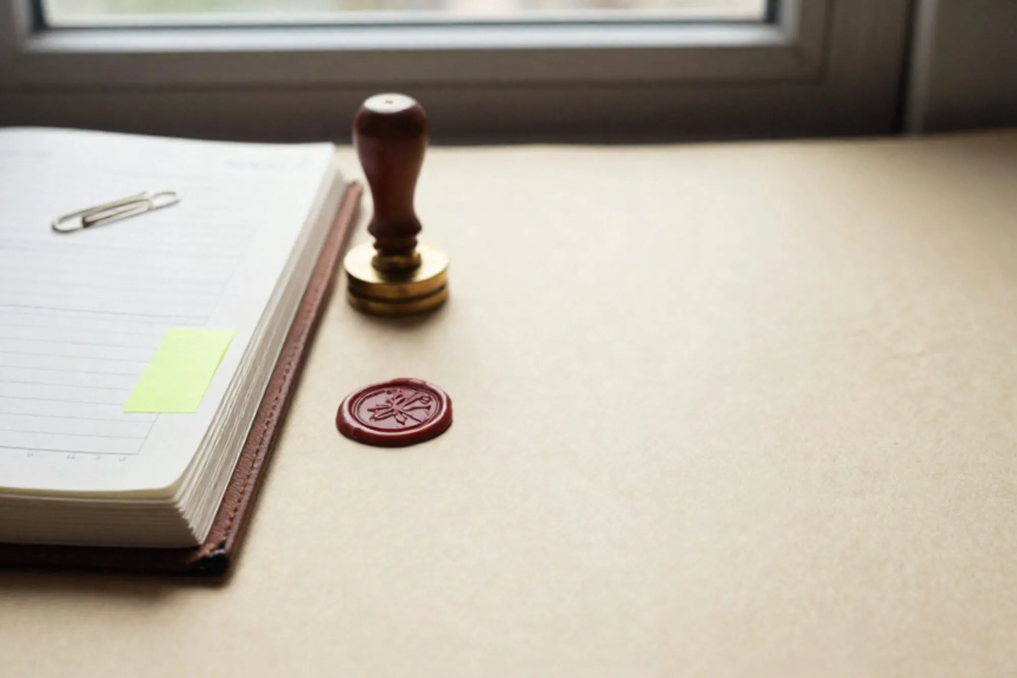 Open leather ledger, bank statement with green tab, brass paperclip, rubber stamp, red wax seal on ivory paper.