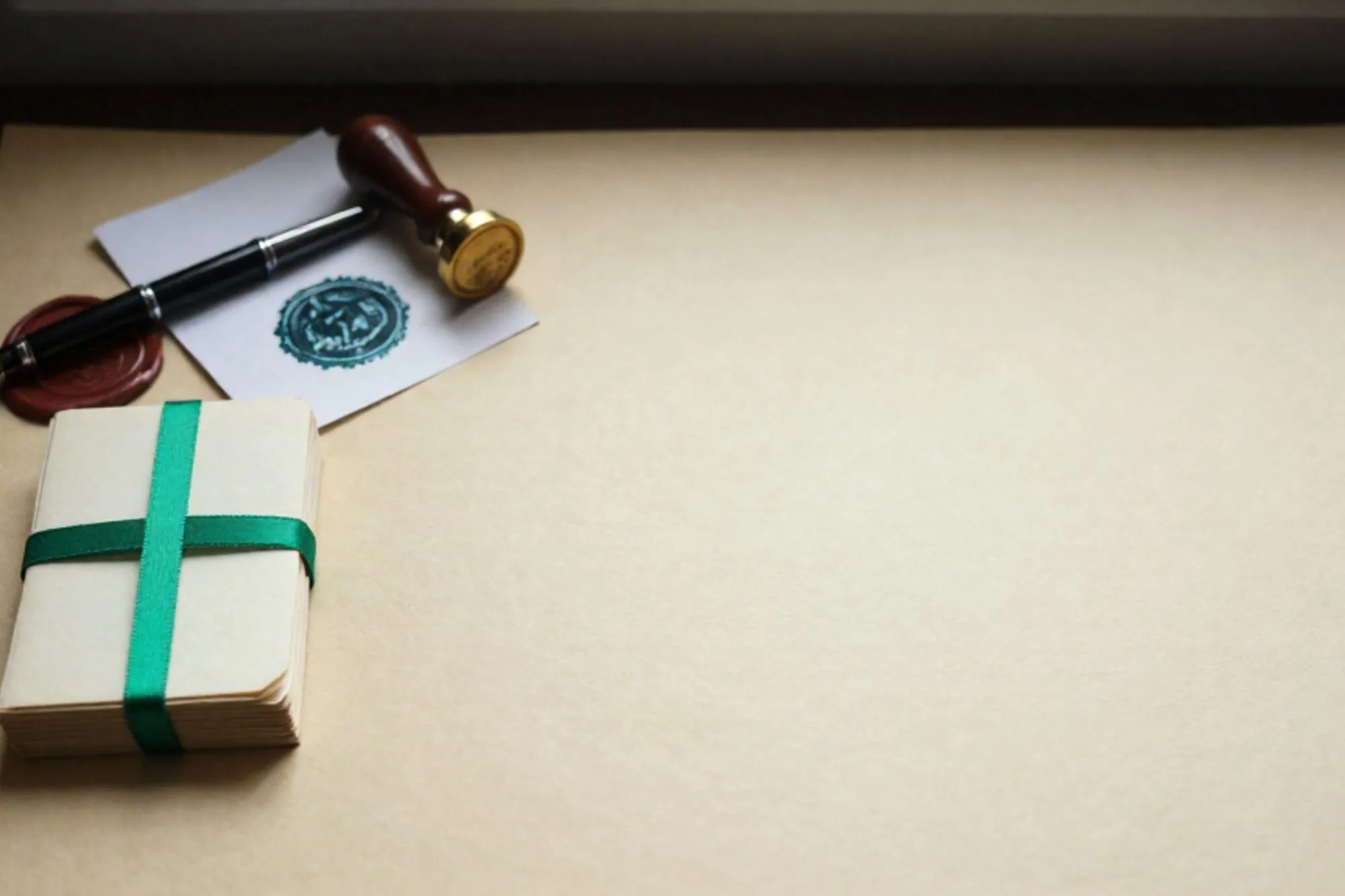 Stapel crème indexkaarten met groen lint, vulpen op leren onderlegger, koperen stempel en lakzegel op ivoren bureau.
