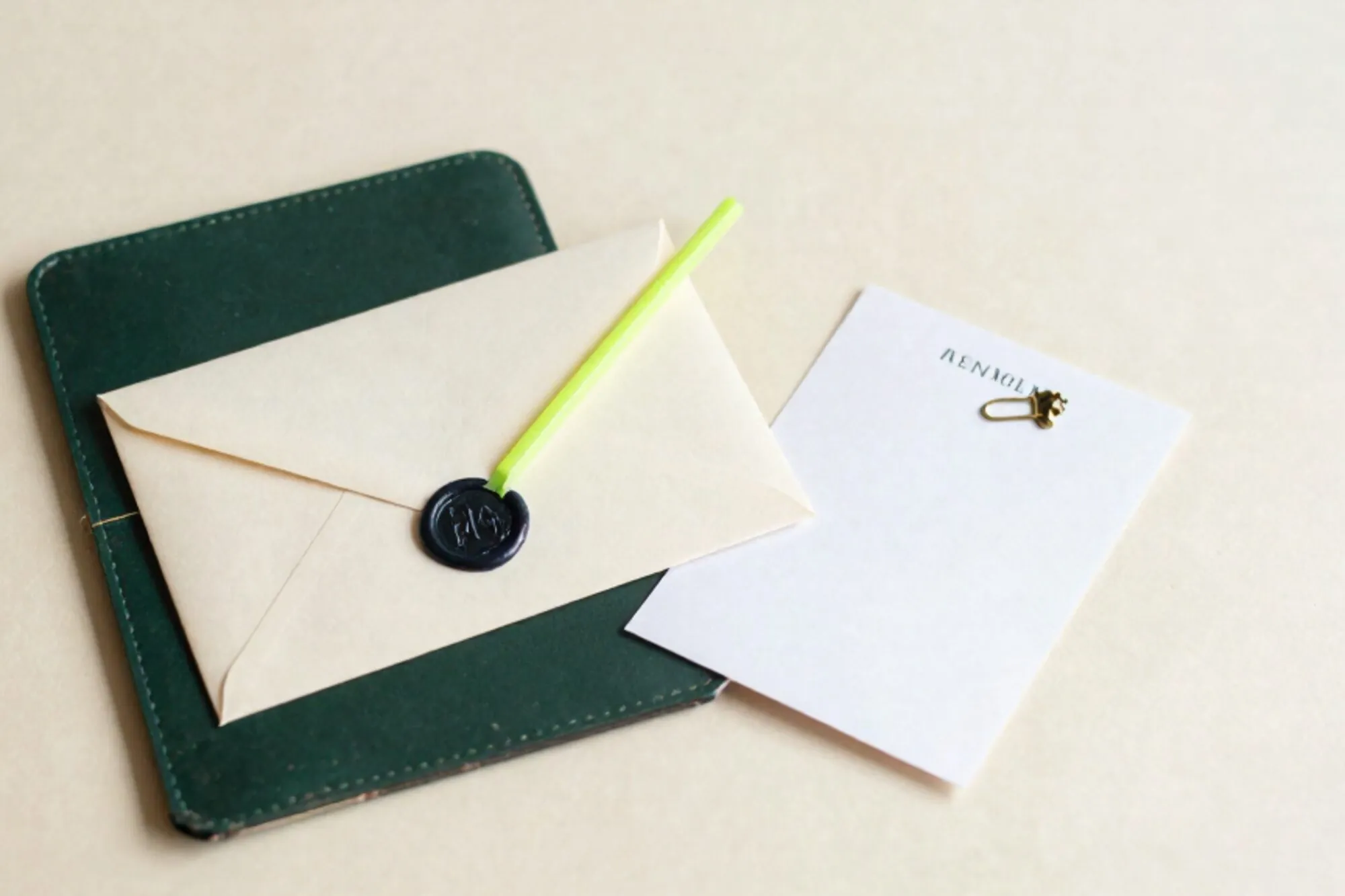 Cream envelope with dark green wax seal on forest leather blotter, green ribbon, brass clip, folded carbon slip.
