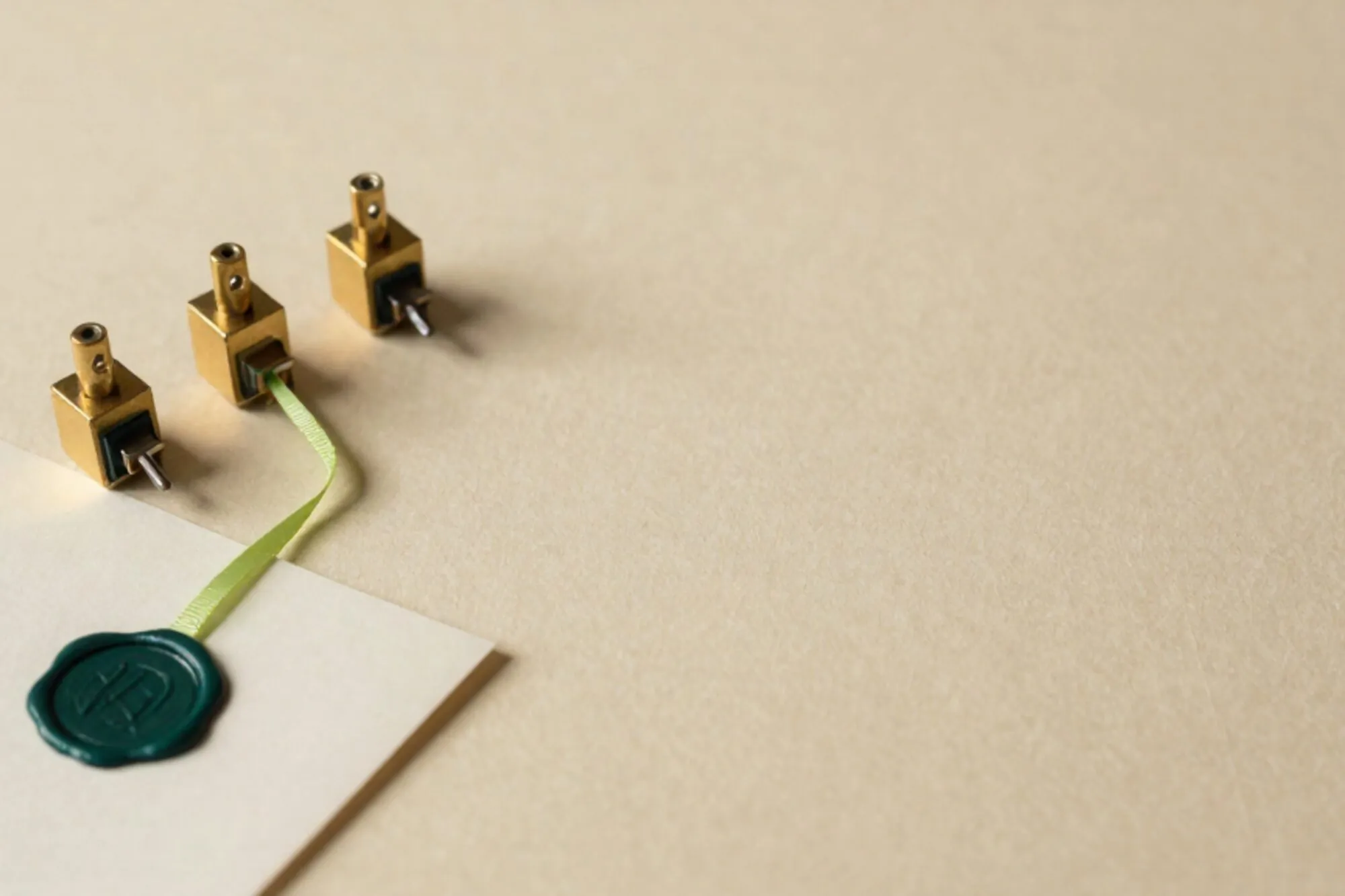 Three brass relay switches on ivory paper with green ribbon and folded slip sealed in dark green wax.