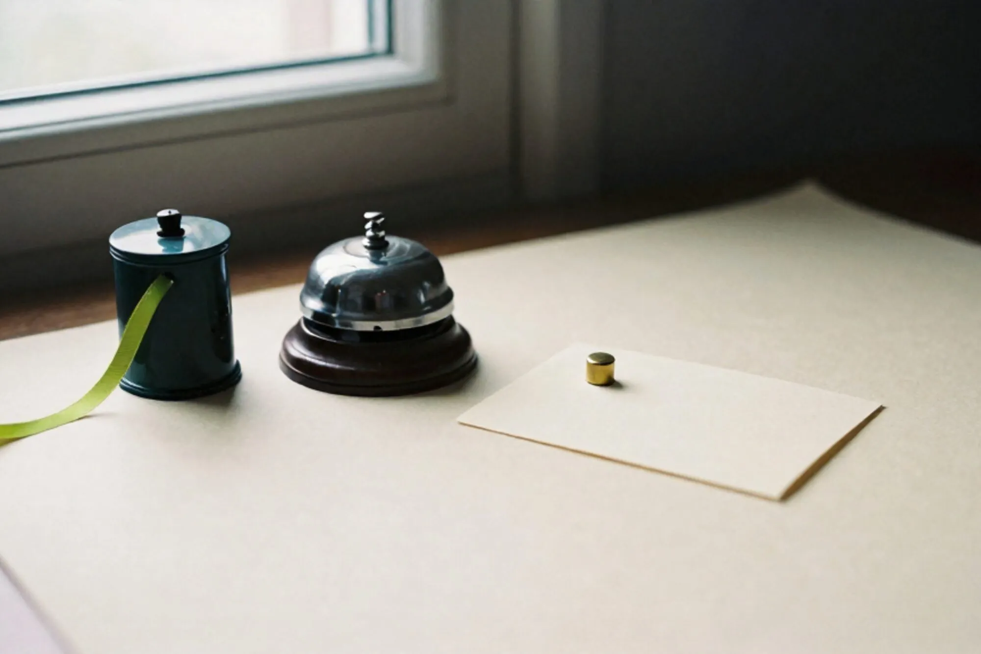 Wooden hotel bell, brass call-button on cream card, green ribbon from pneumatic tube on ivory paper.