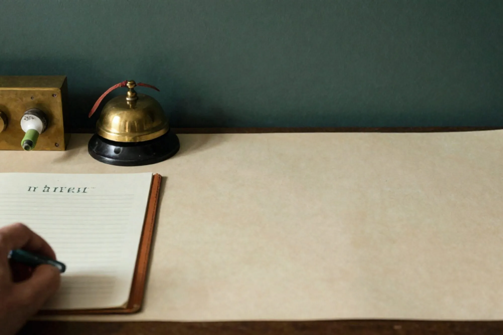 Brass call-annunciator panel with green tab, paper slip, leather blotter and brass bell on an ivory desk.