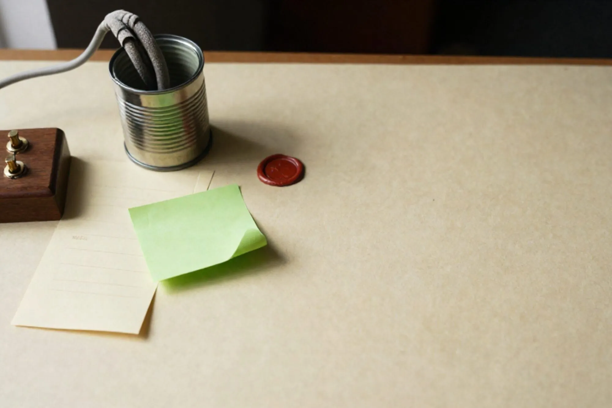 Wooden switchboard with brass jacks, fabric cable in pneumatic tube canister, paper form, green sticky note on ivory desk.