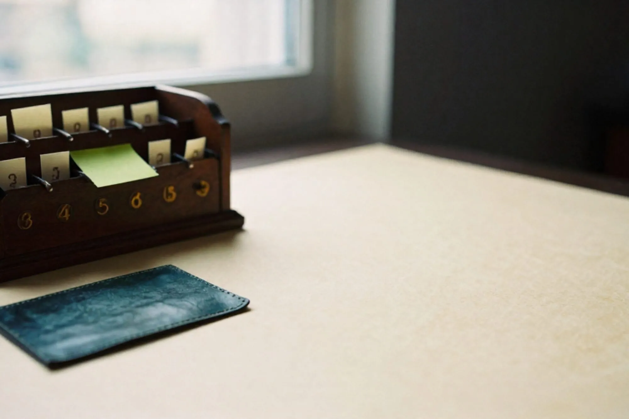Houten hotelpostvak met messing vakjes vol crème briefjes en één groene sticky note op een leren onderlegger.