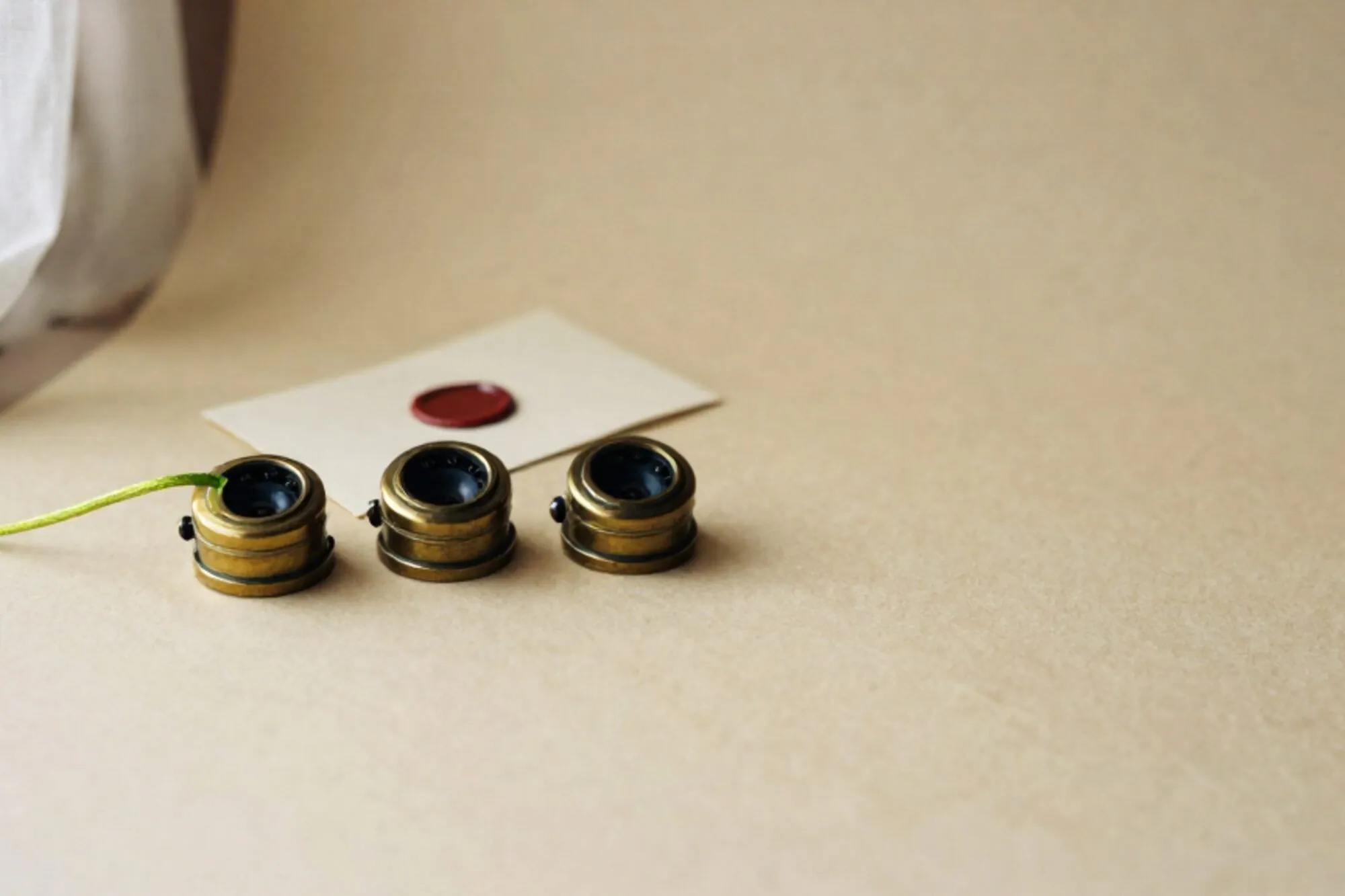 Three brass switchboard jacks in a row on ivory paper, green silk cord looping across, folded card with red wax dot.
