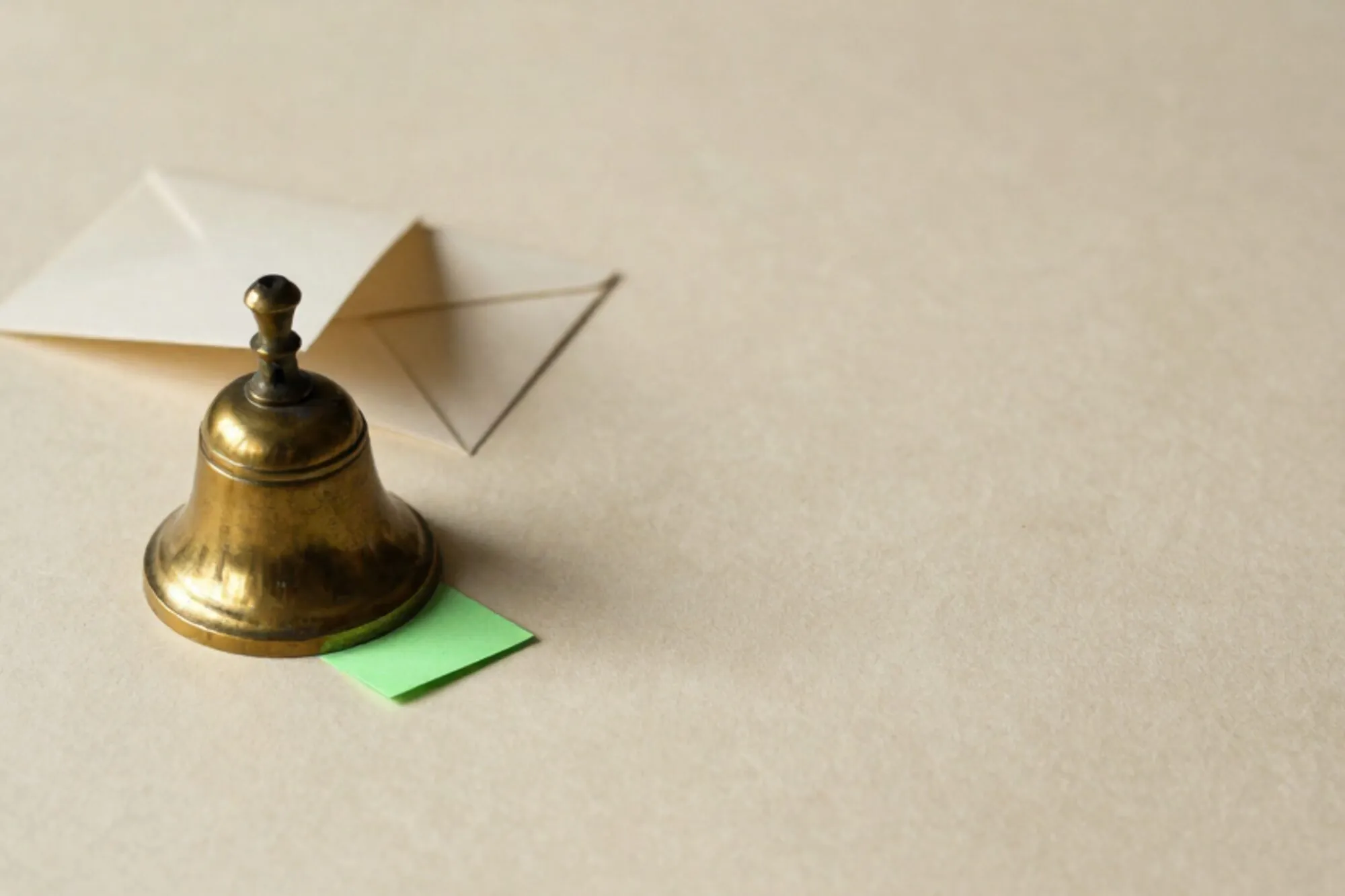 Messing baliebel op ivoorkleurig papier met groene indexkaart eronder en crèmekleurige envelop erachter, links in beeld.