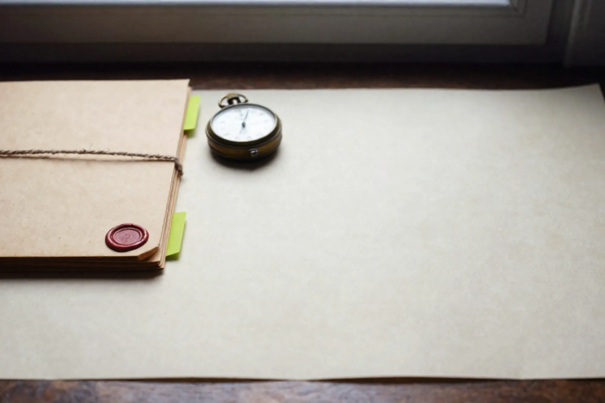 Weathered manila dossier tied with linen twine, green index tab, brass stopwatch face-down on ivory paper desk.