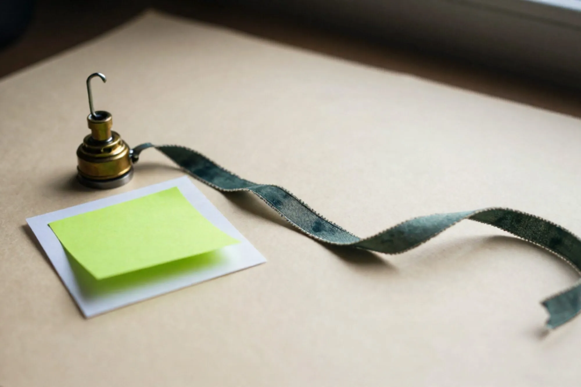Messing relais, gevouwen papierstrook met groen plakkertje, linnen lint op ivoorkleurig papier.