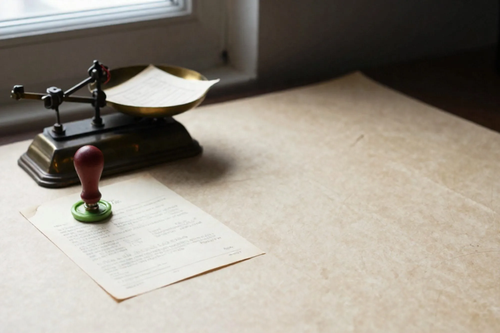 Antique brass postal scale on ivory paper desk, cream invoice on pan, chartreuse wax seal, red thread on balance arm.