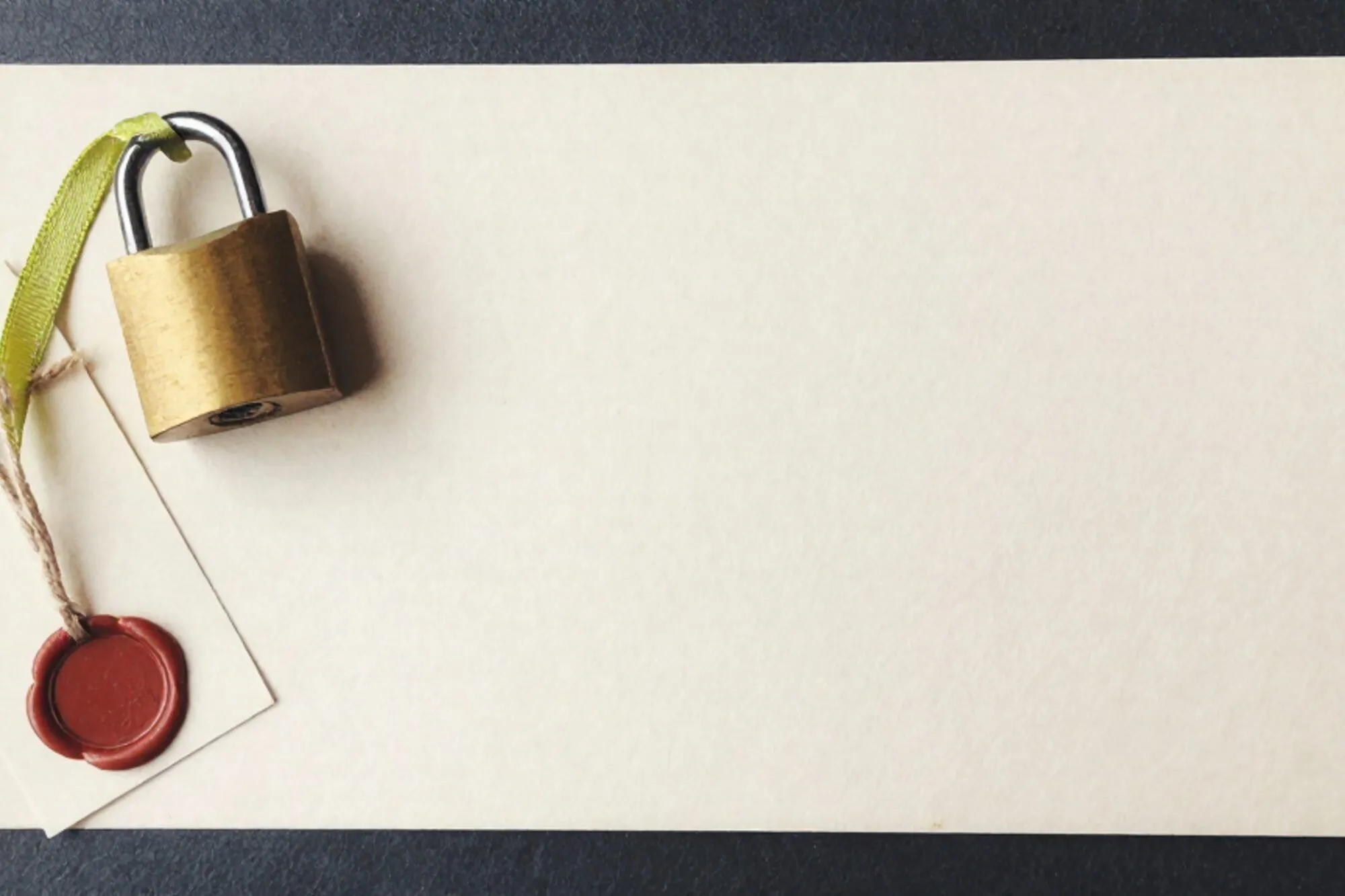 Brass padlock on cream index card with green silk ribbon, paper tag on linen twine, red wax seal, ivory blotter.