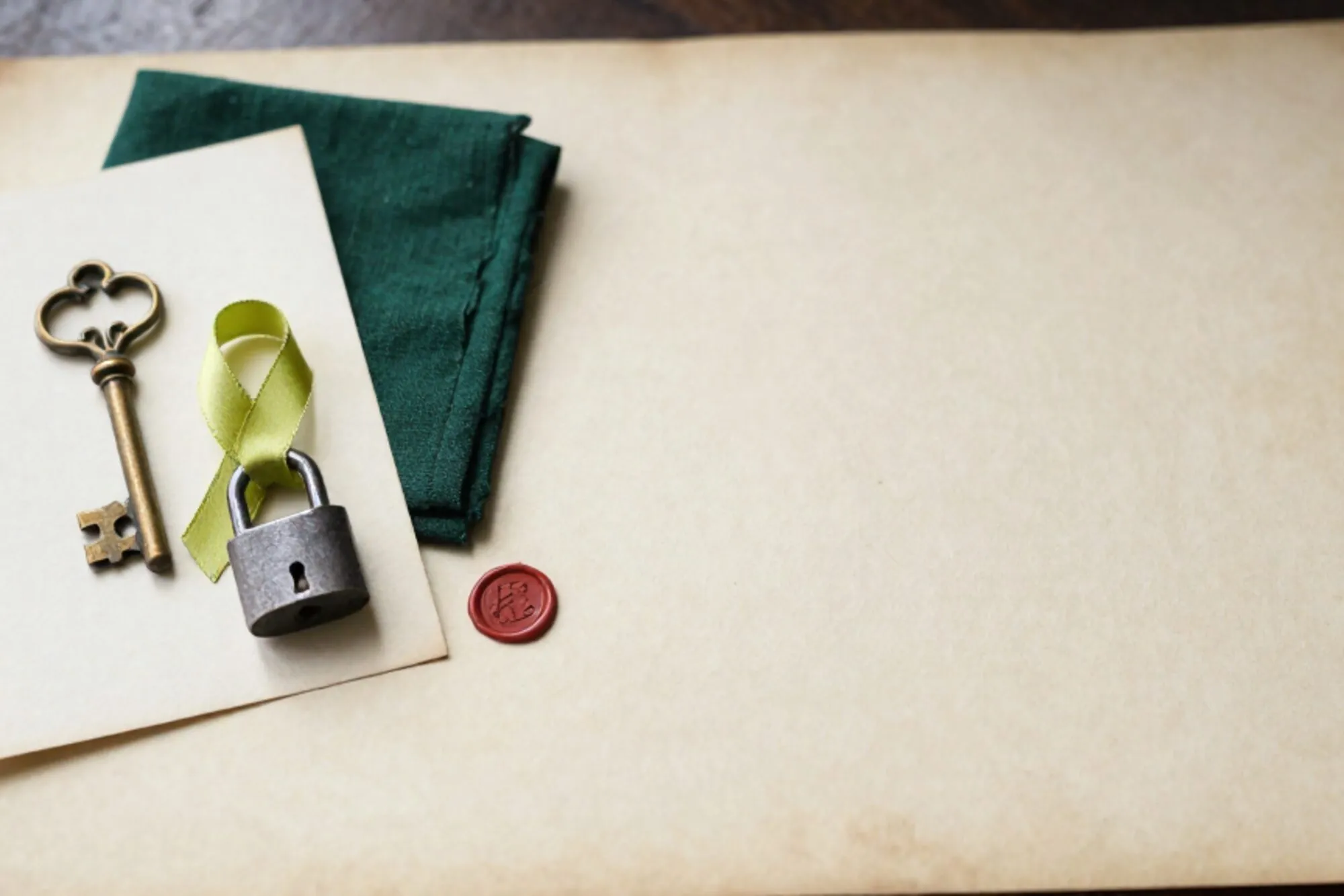 Messing sleutelplaat en klein ijzeren hangslot op crème indexkaart, groen zijden lint door het slot, ivoorkleurig papier.