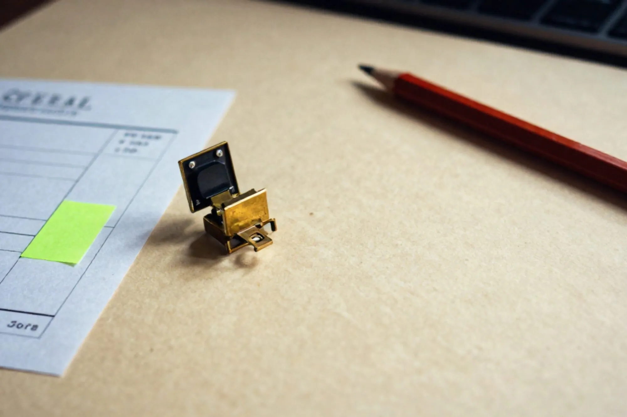 Brass relay switch tripped open beside a folded paper invoice with a green sticky note and red wax pencil on ivory.