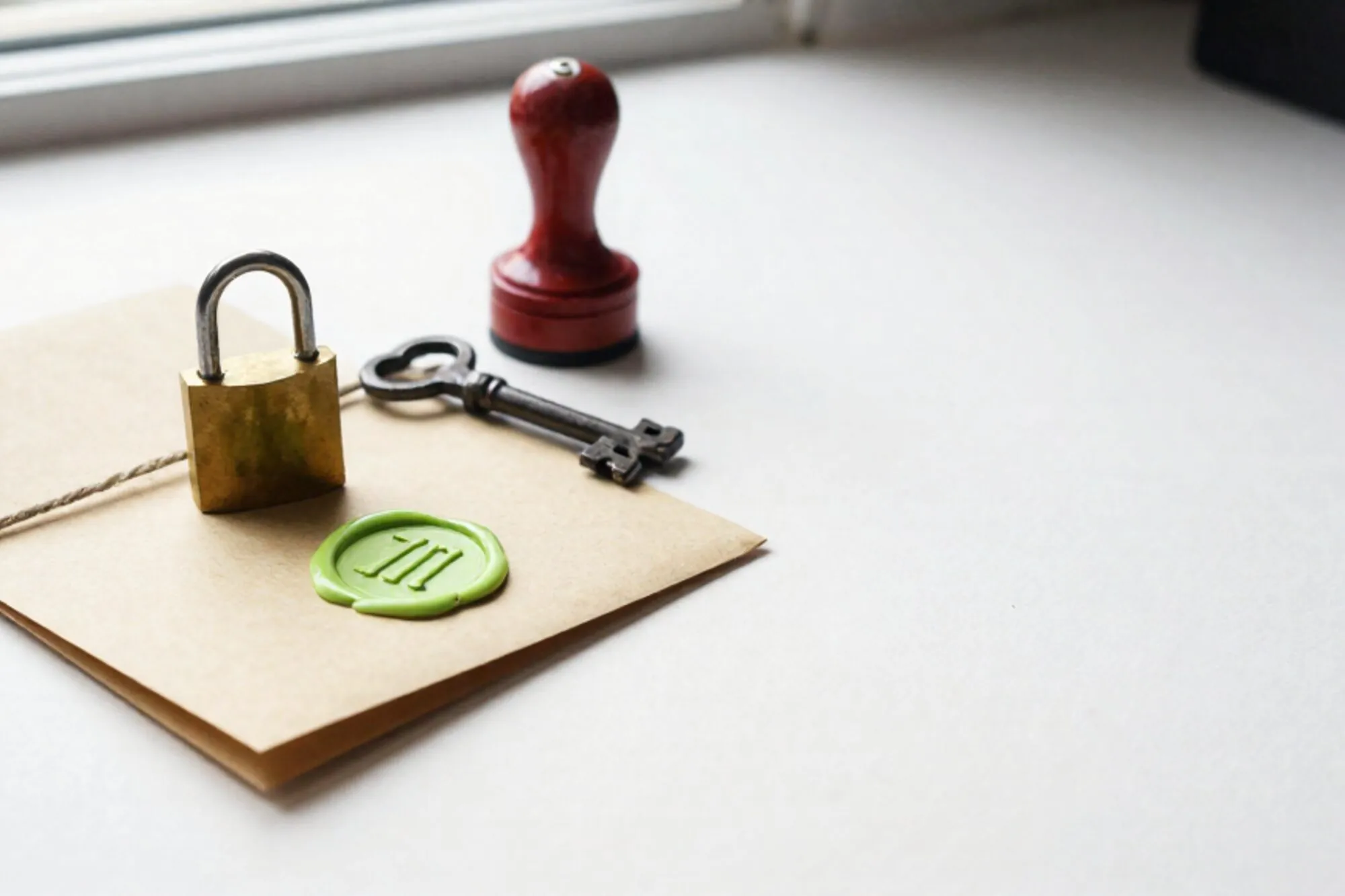 Brass padlock on manila folder tied with linen string, green wax seal, iron key, red rubber stamp on ivory paper.