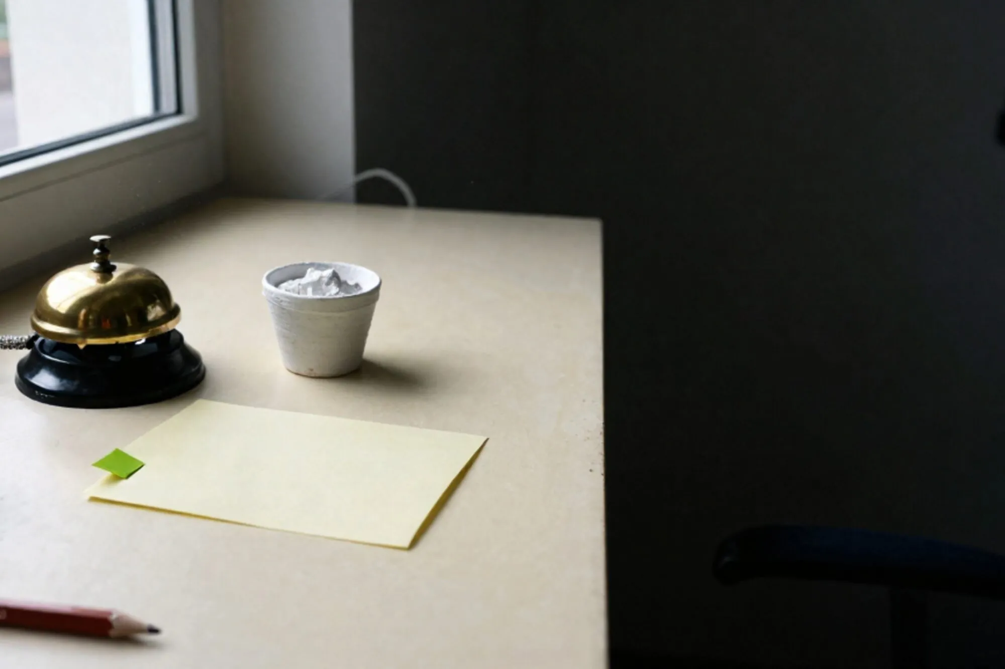 Brass hotel-bell switchboard, cream order slip with green tag, cup of plaster powder, brass coil, red wax pencil on ivory desk.