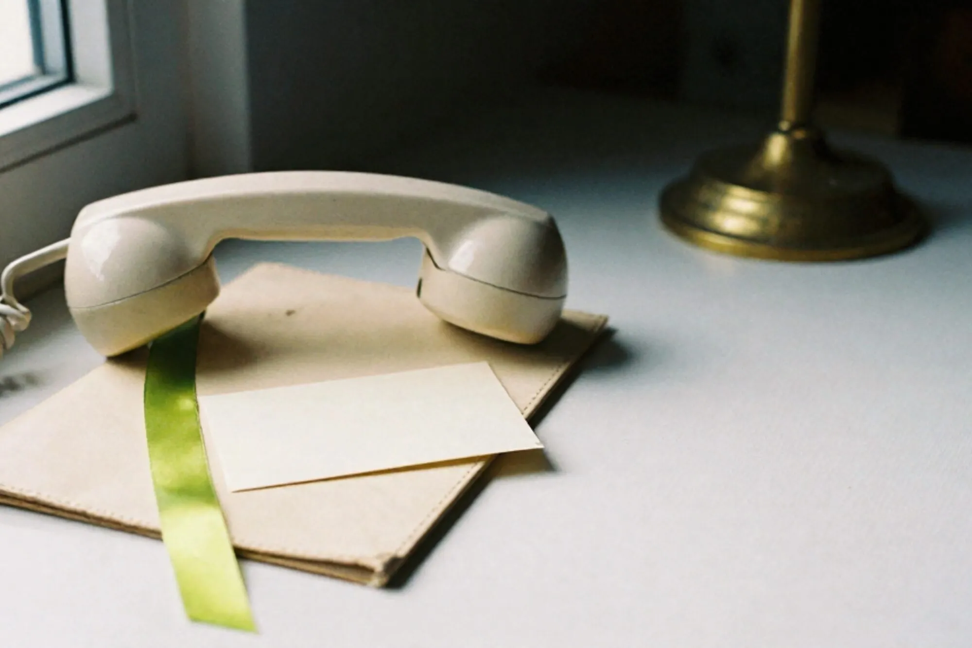 Cream bakelite phone receiver off-hook on ivory leather blotter, green ribbon, brass cradle, appointment card.