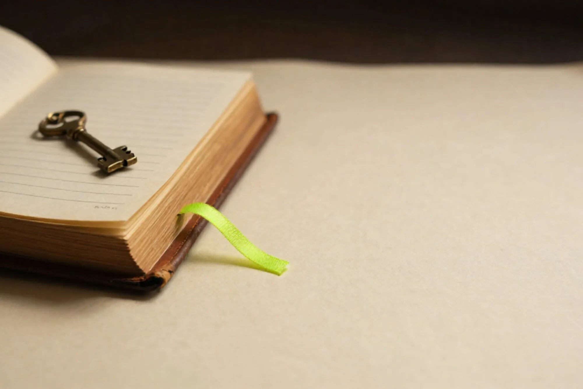 Open leren logboek met koperen sleutel op crème kaart en limegroen lint, op ivoorkleurig papier.