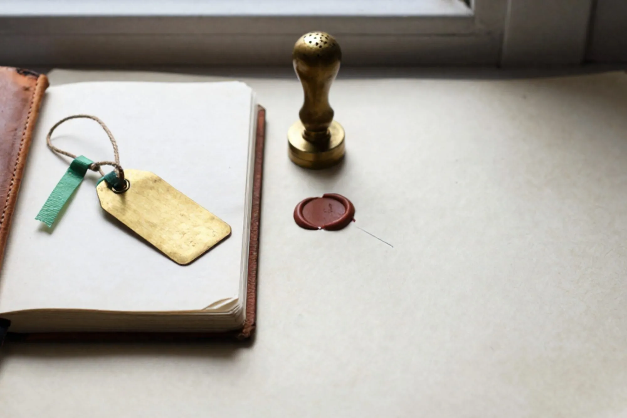 Open leather logbook with brass shipping tag, green ribbon, ink stamp, red wax fragment on ivory paper.