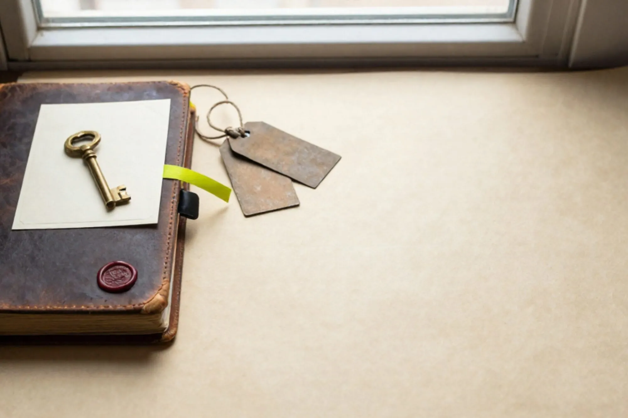 Leather logbook, brass key on card, iron tags with twine, green ribbon, red wax fragment on ivory paper.