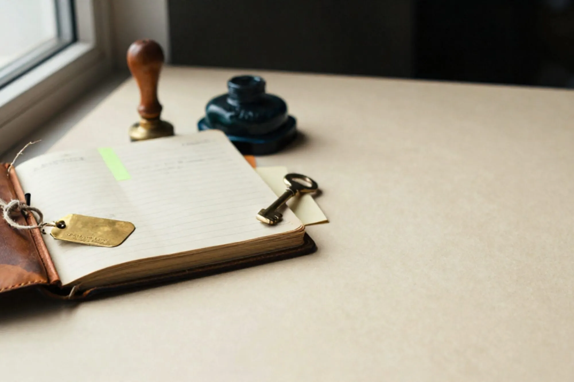 Open leather customs logbook, brass shipping tag on linen twine, green sticky tab, rubber stamp, ink pad, brass key on ivory paper.