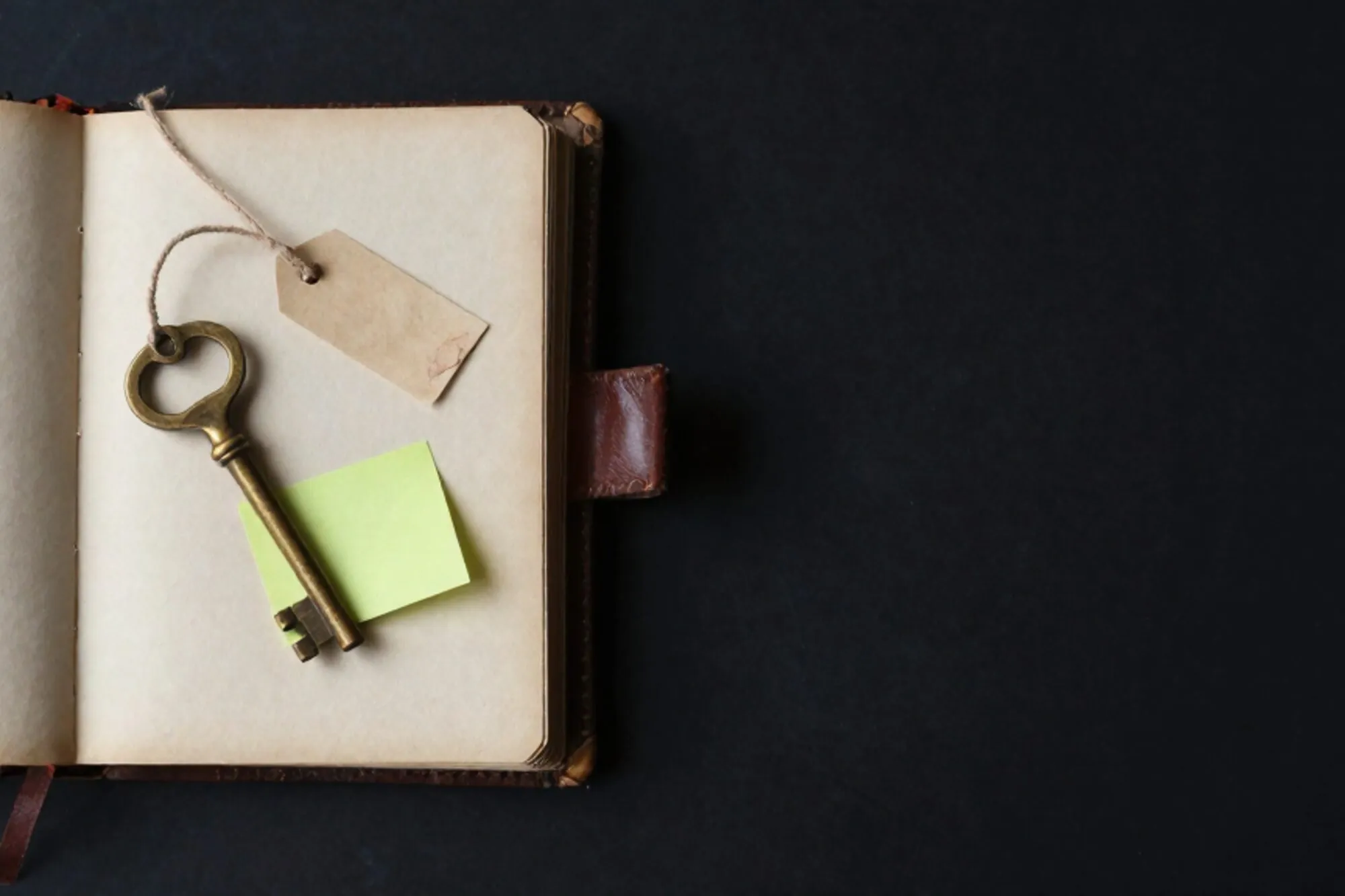 Open leather logbook on ivory paper with brass key, linen-tied iron tag, chartreuse sticky note, red wax fragment.