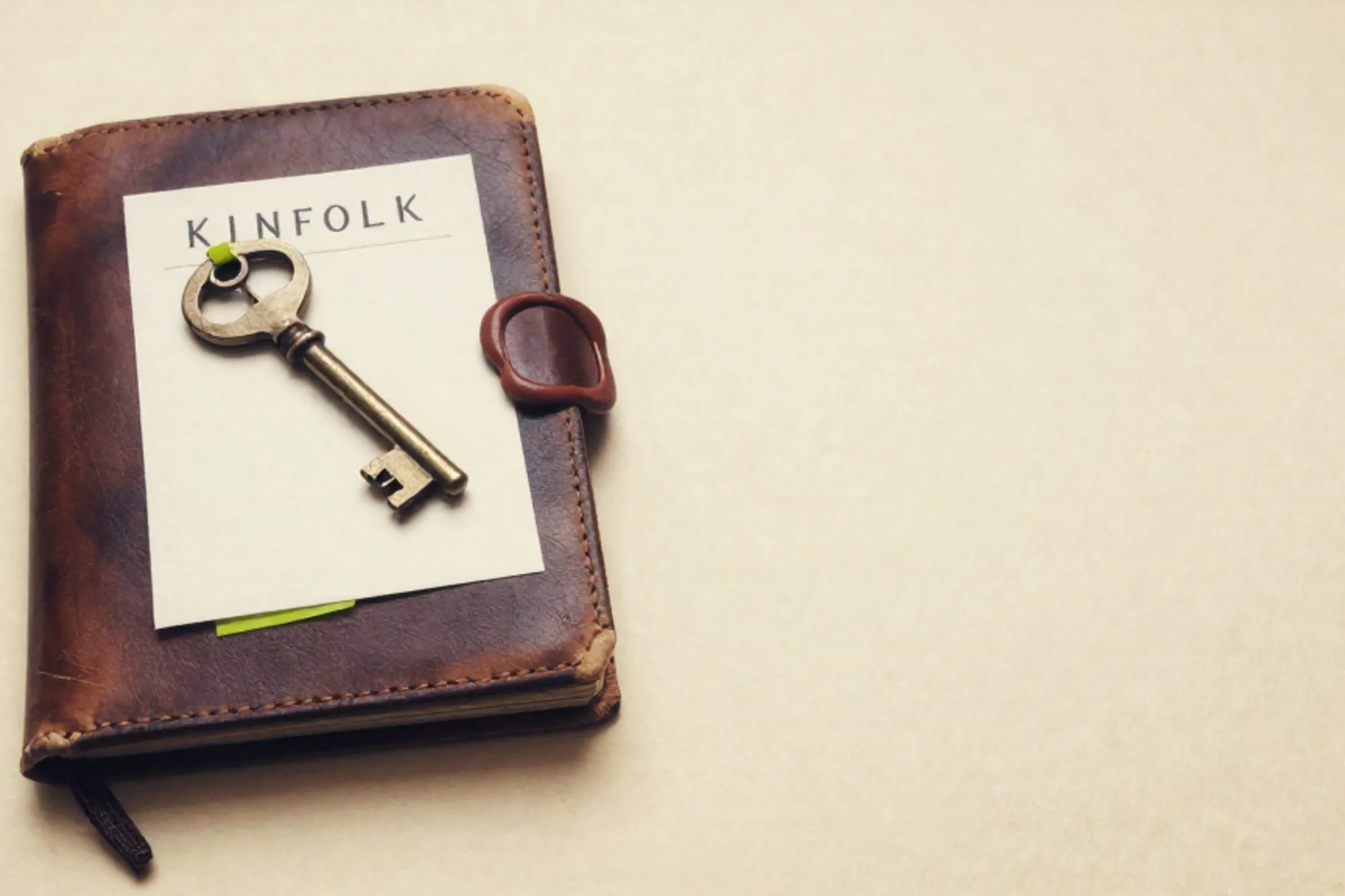 Closed leather logbook with brass key on cream card, green ribbon, red wax fragment on ivory paper.
