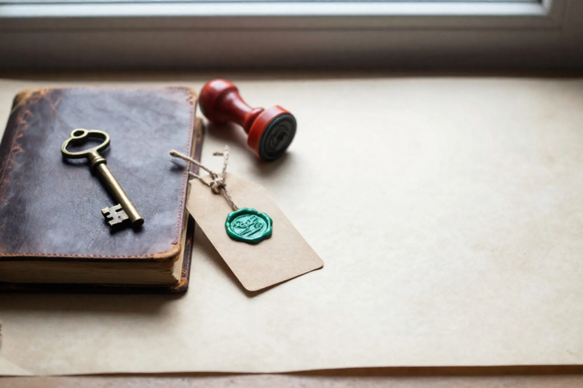Closed leather logbook with linen bookmark, brass key on cover, manila tag with green wax seal, red rubber stamp on ivory paper.