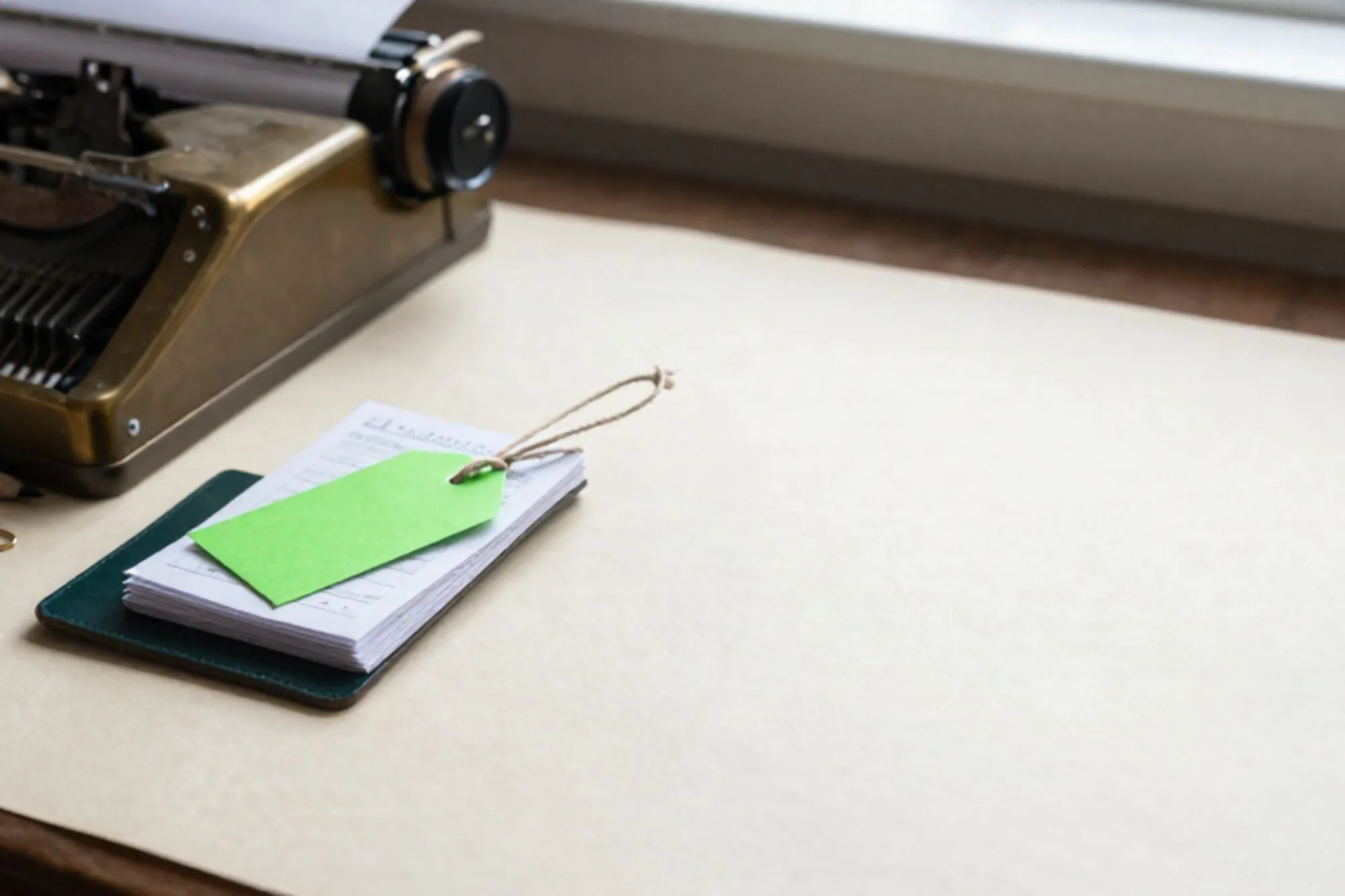 Brass adding machine, carbon receipt slips, green paper tag on linen string, leather blotter, paperclip, pencil stub.