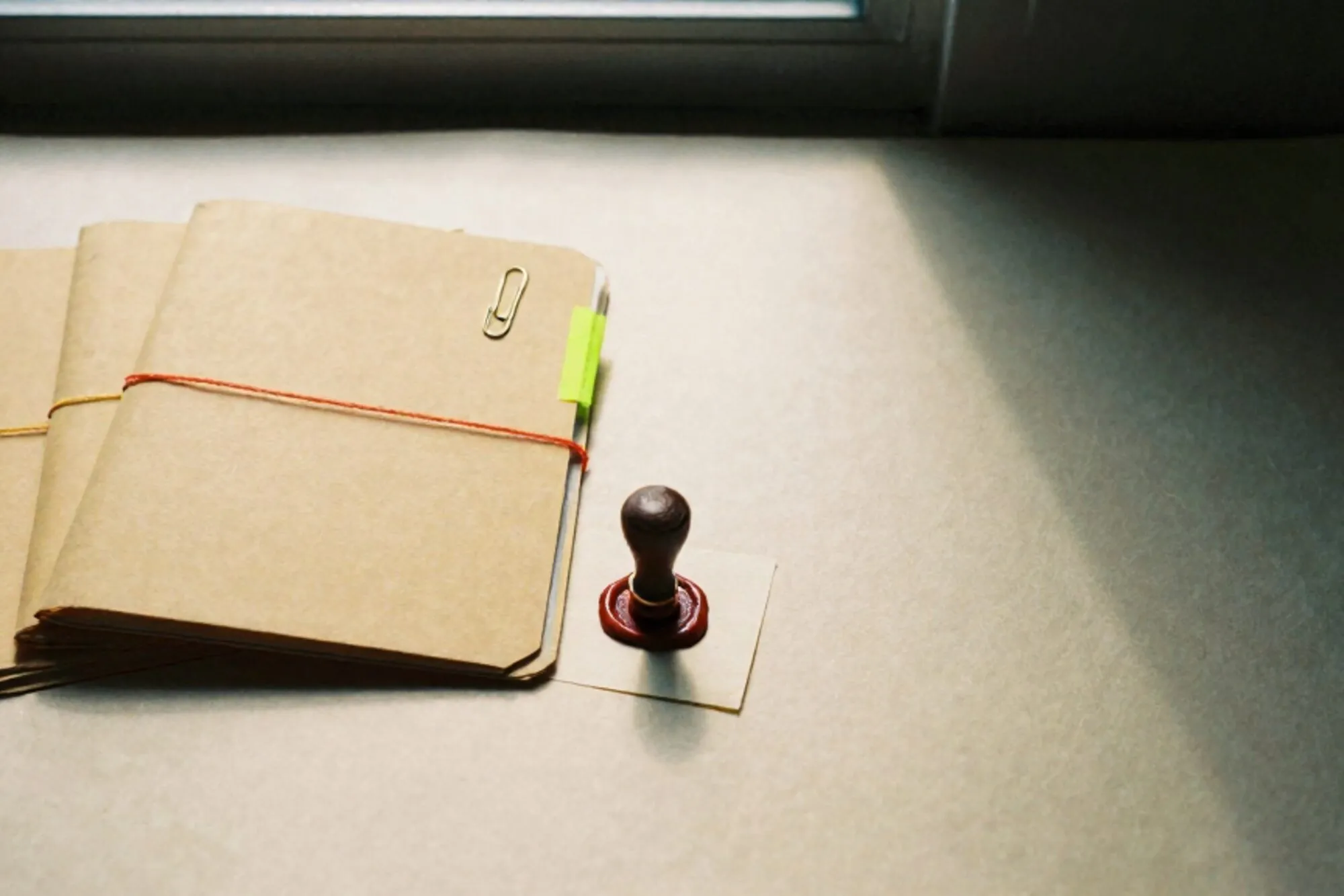 Three manila folders tied with coloured thread on ivory paper, chartreuse tab, brass clip, red wax seal, side light.