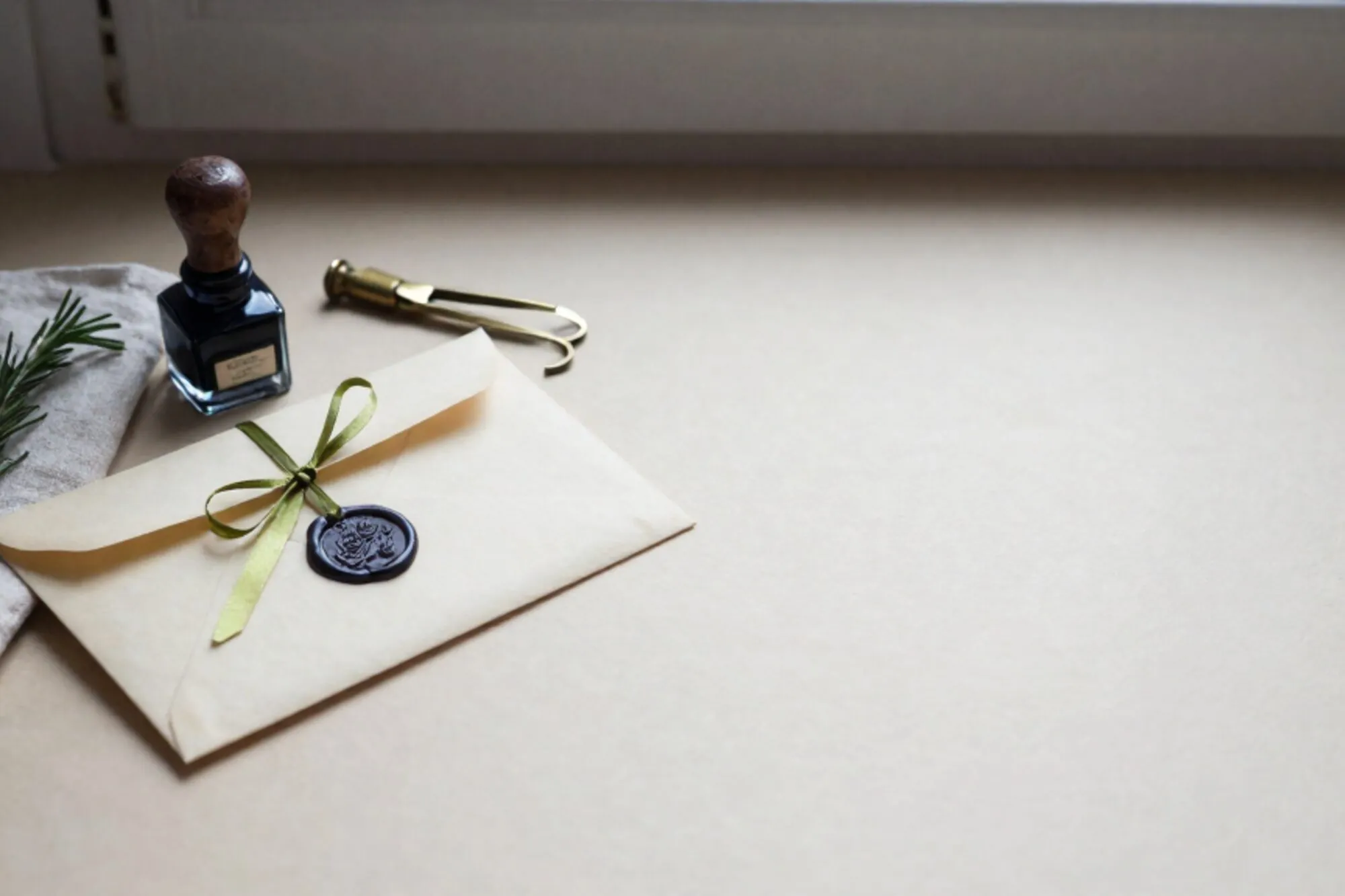 Crème envelop met groene lakzegel en limoenlint, linnen zakdoek, rozemarijntakje, messing briefopener op ivoorkleurig papier.