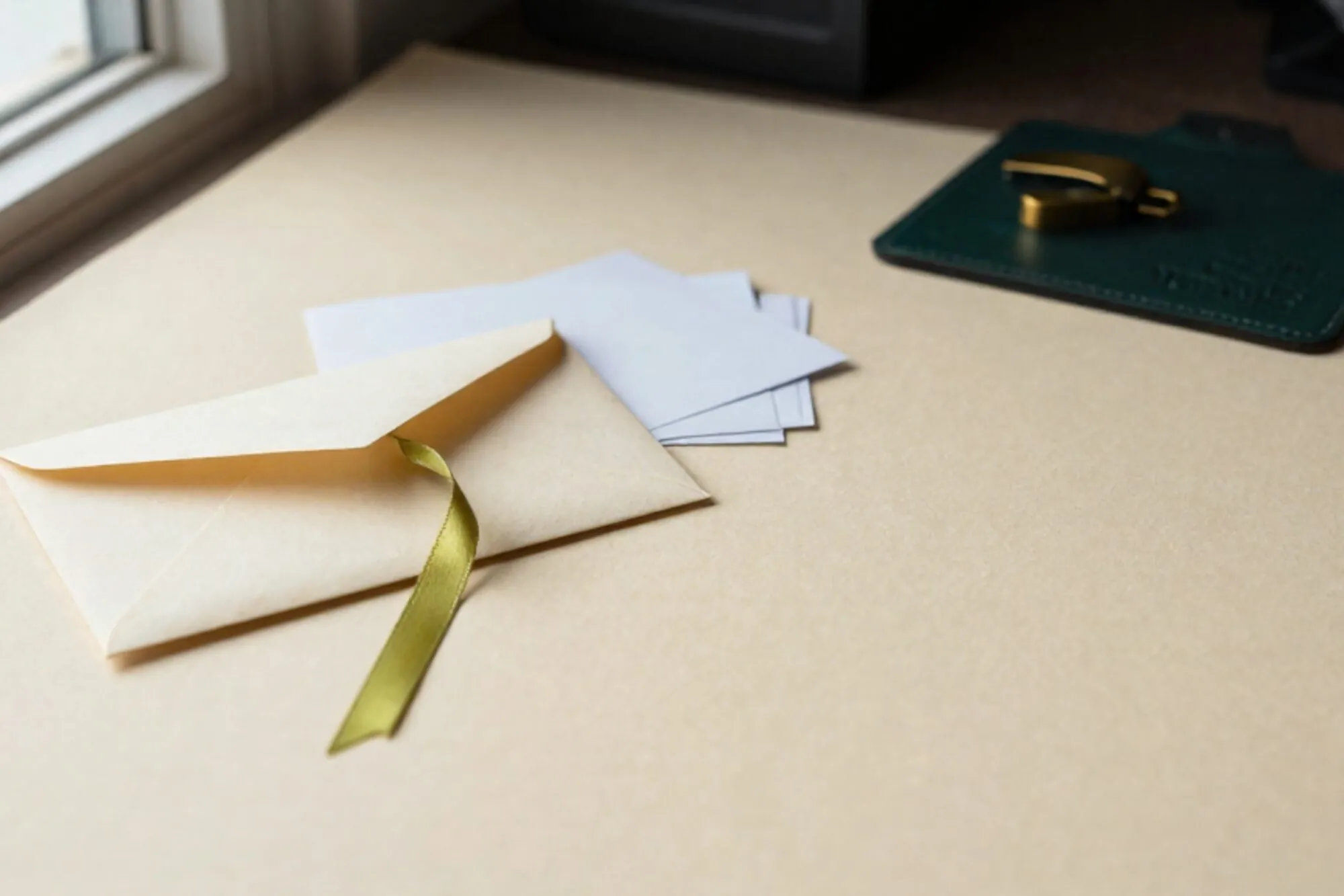 Crèmekleurige envelop met groen lint, carbonpapier-strookjes, koperen briefopener op donkergroene leren onderlegger.