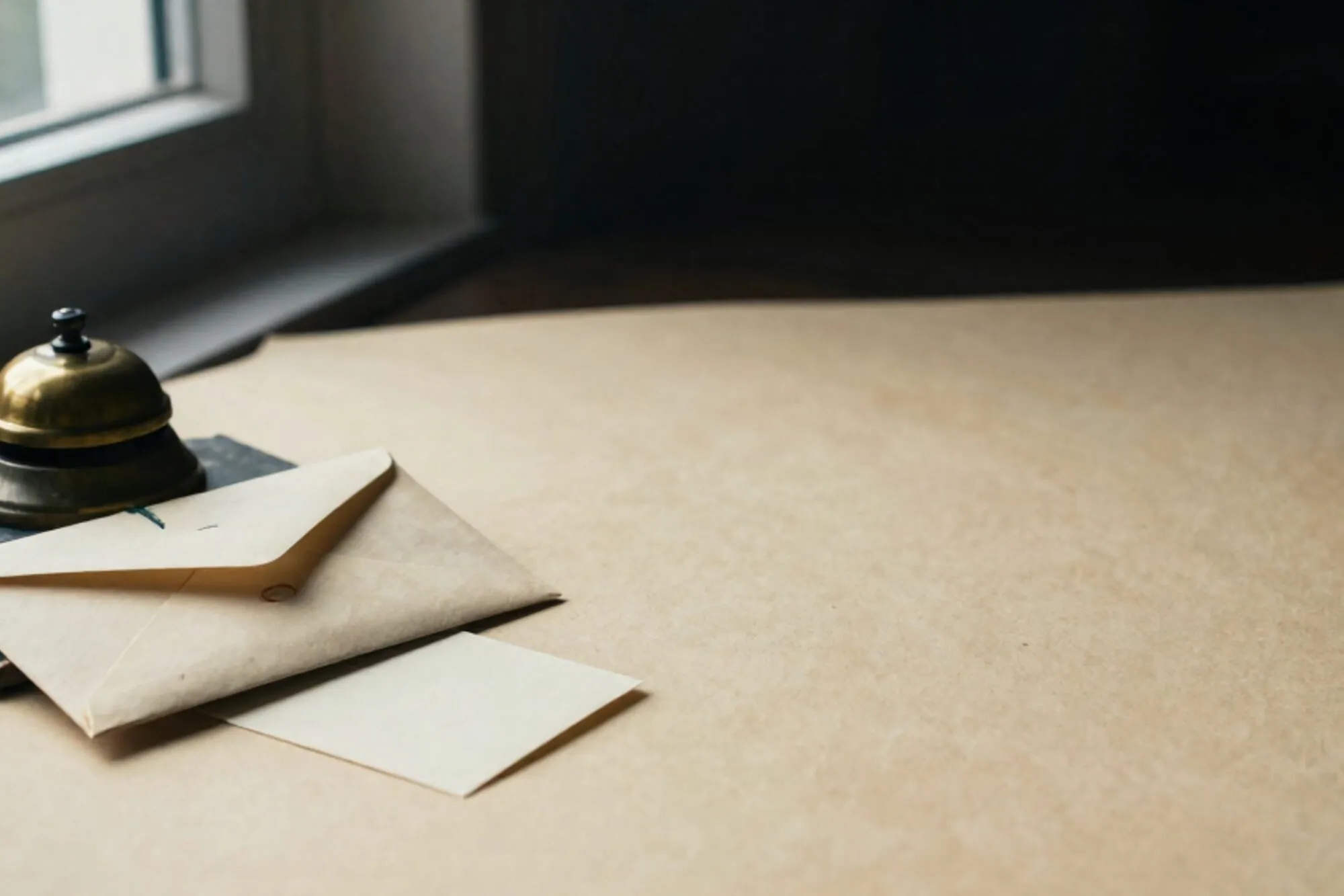 Sealed manila envelope with chartreuse ribbon on dark blotter, brass bell and cream index card on ivory desk.