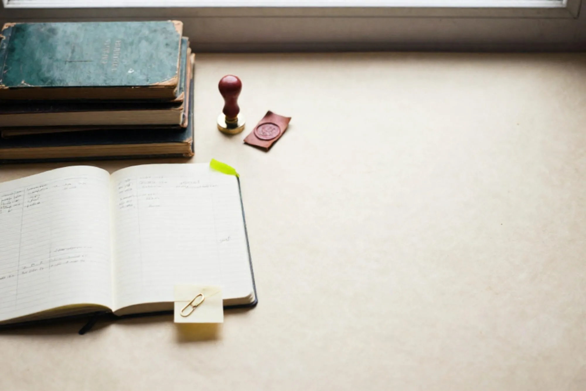 Stacked manila ledgers on ivory paper, open ledger with Dutch invoice columns, brass paperclip, green tab, wax seal.