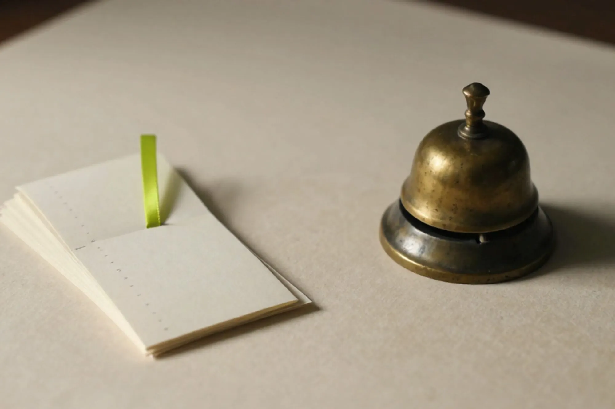 Brass desk bell, fanned cream receipts with chartreuse ribbon and vintage clip on linen blotter, side light.