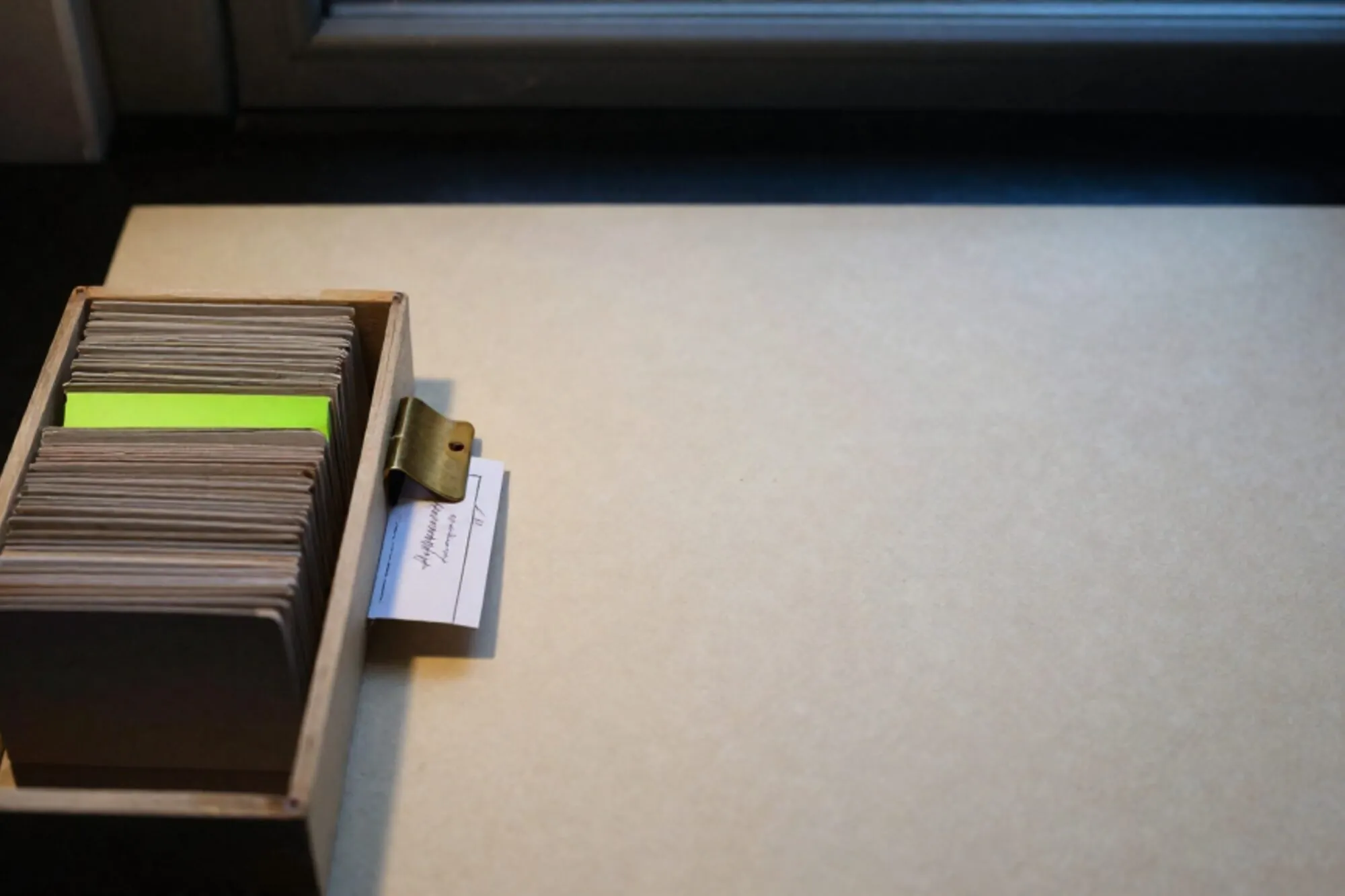 Open index-card drawer on ivory desk blotter, manila cards fanned with one chartreuse tab card and brass divider.