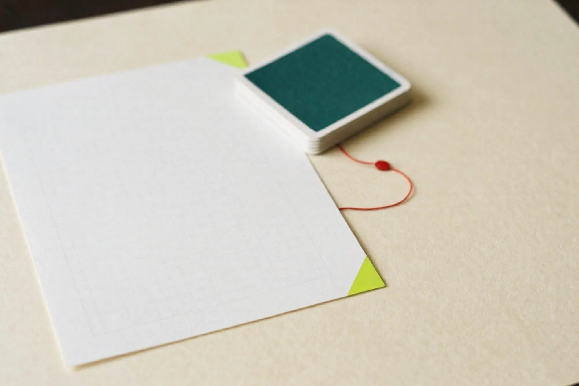 Letterpress proof sheet with green index tab, forest-ink colour cards, pencil grid, red thread on ivory paper.
