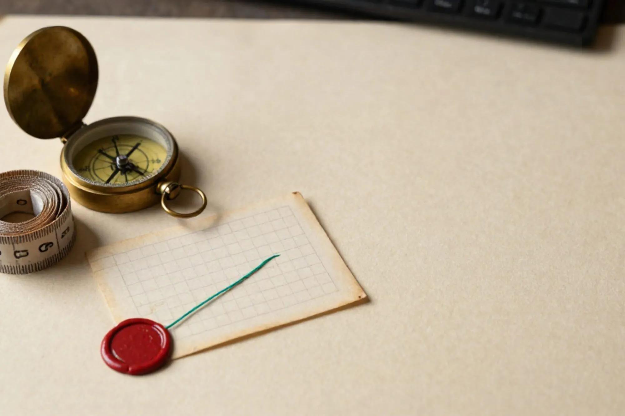 Brass compass, linen tape, cream index card with green thread and red wax seal on ivory paper.