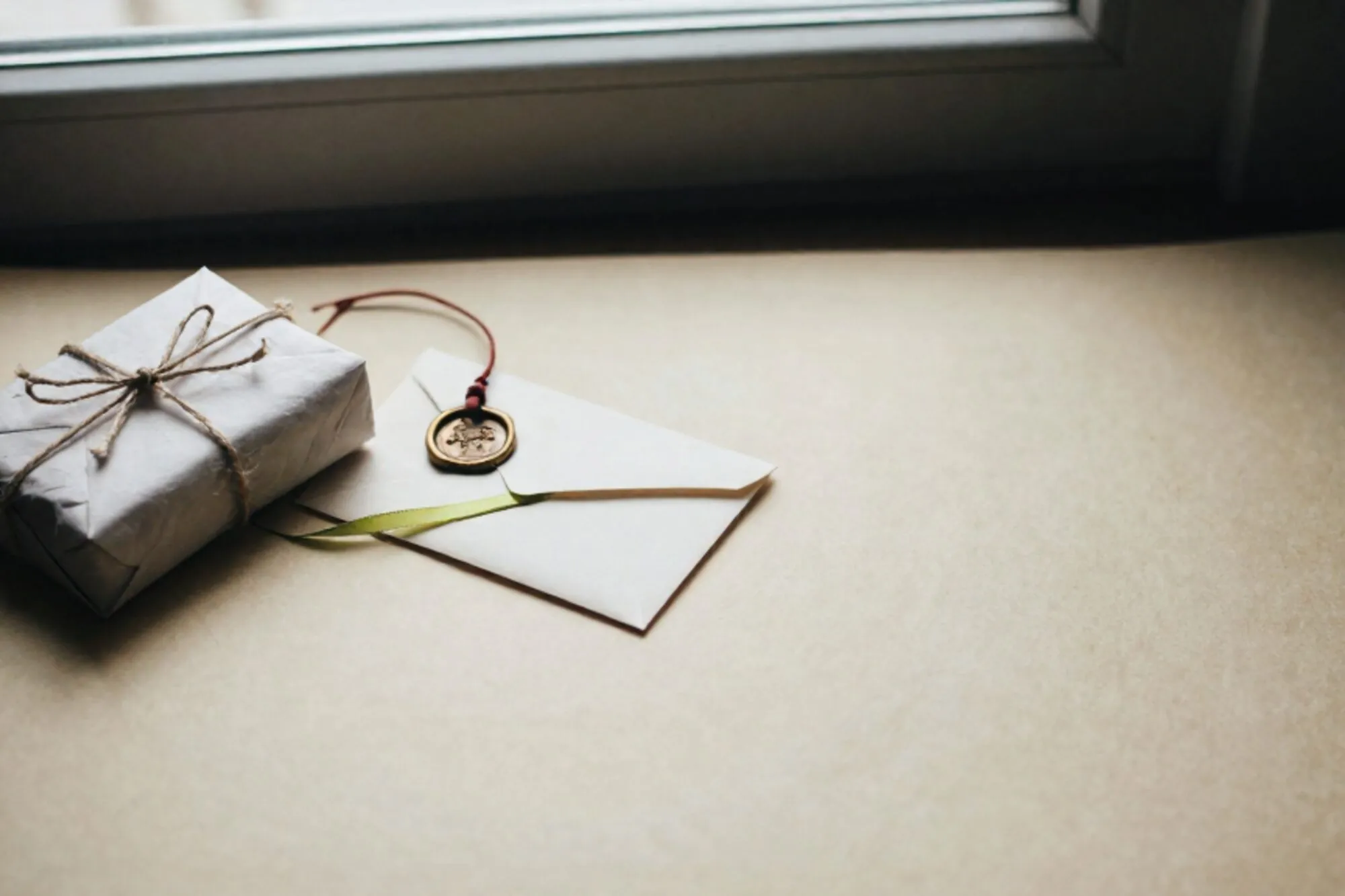 Small craft-paper parcel with linen twine, wax-sealed envelope, green ribbon, brass luggage tag on ivory paper.