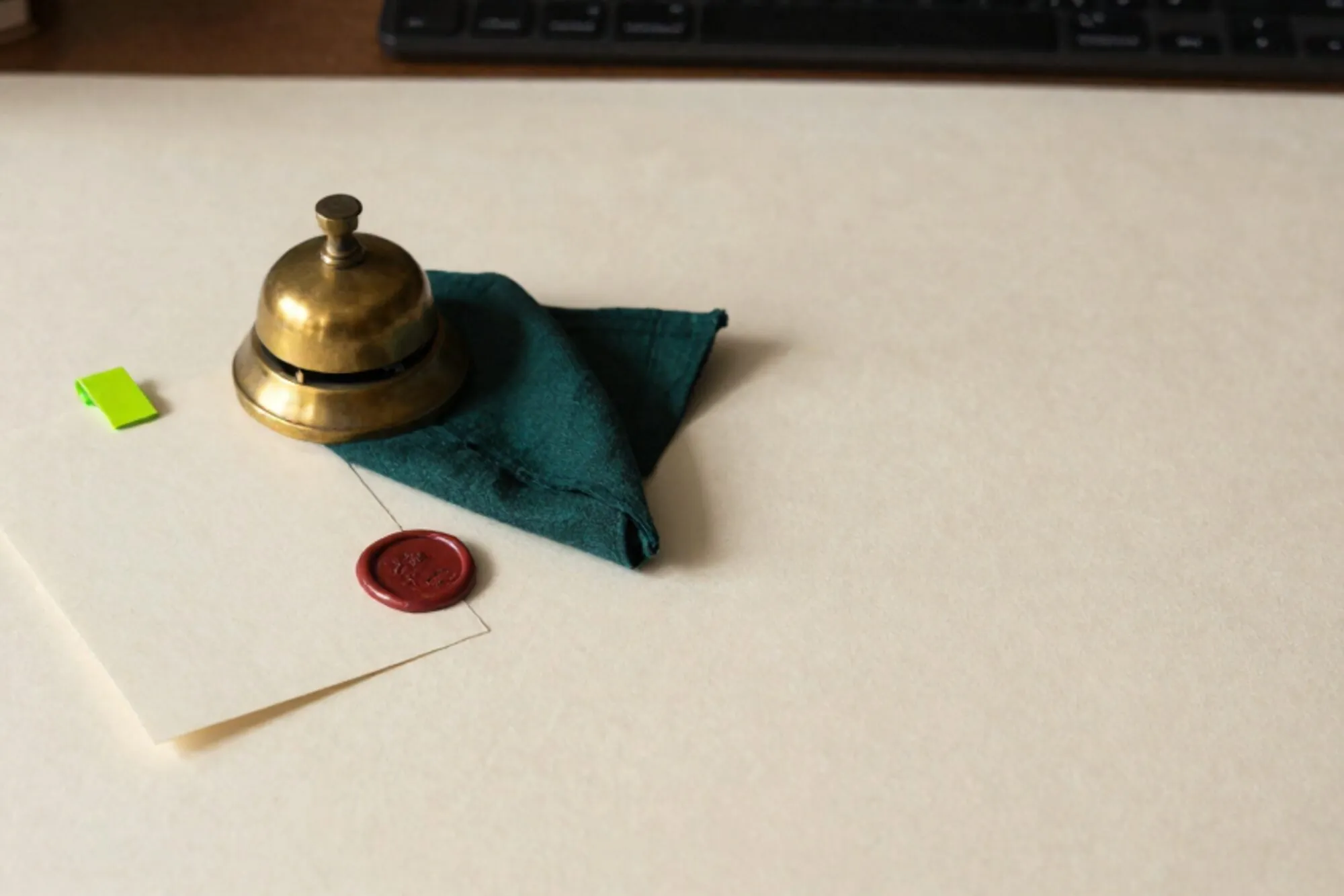 Ivory desk with cream triage card, green flag tab, brass bell, folded ink handkerchief, red wax seal, side light.